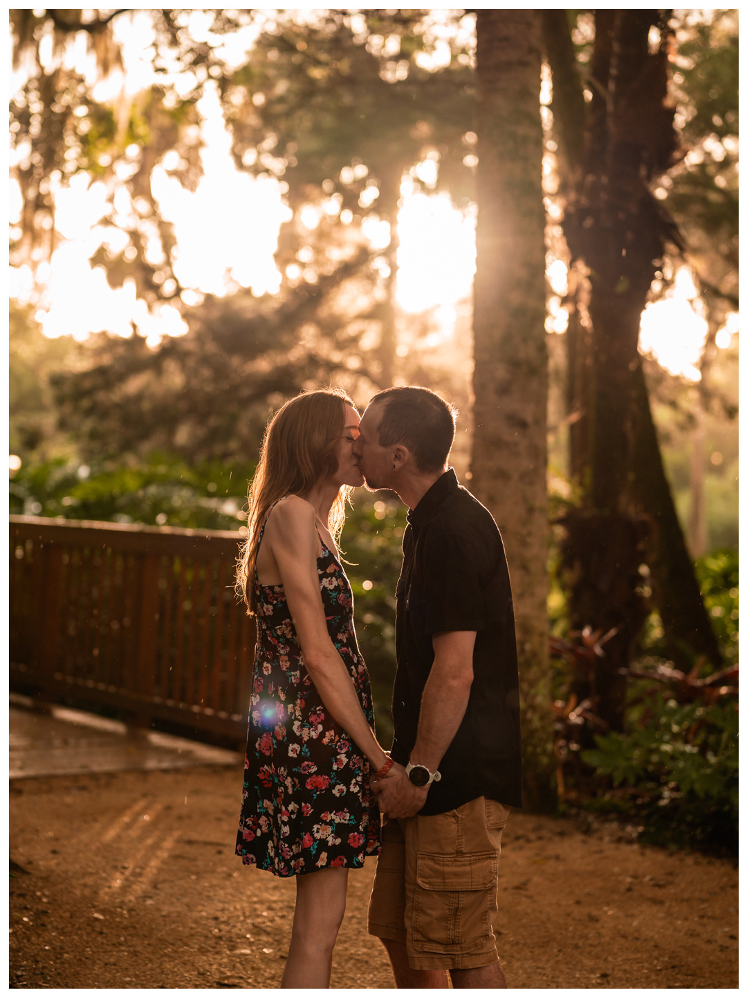 Couple holding hands on a garden path with warm sunlight filtering through the trees at Washington Oaks.