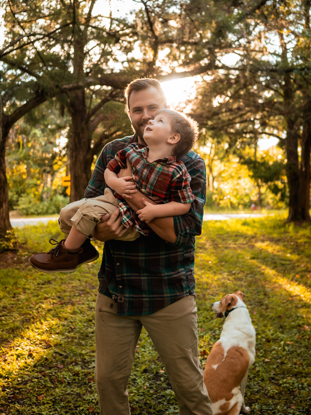 Jon holding David while their dog walks beside them during golden-hour family photos in New Smyrna Beach backyard.