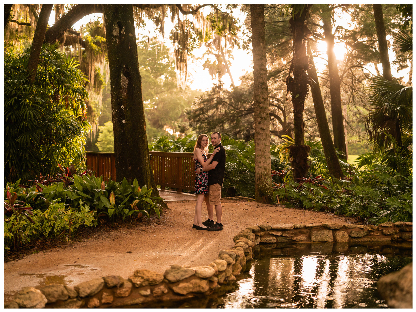 Wide portrait of a couple beside a garden pond beneath the oak trees at Washington Oaks.