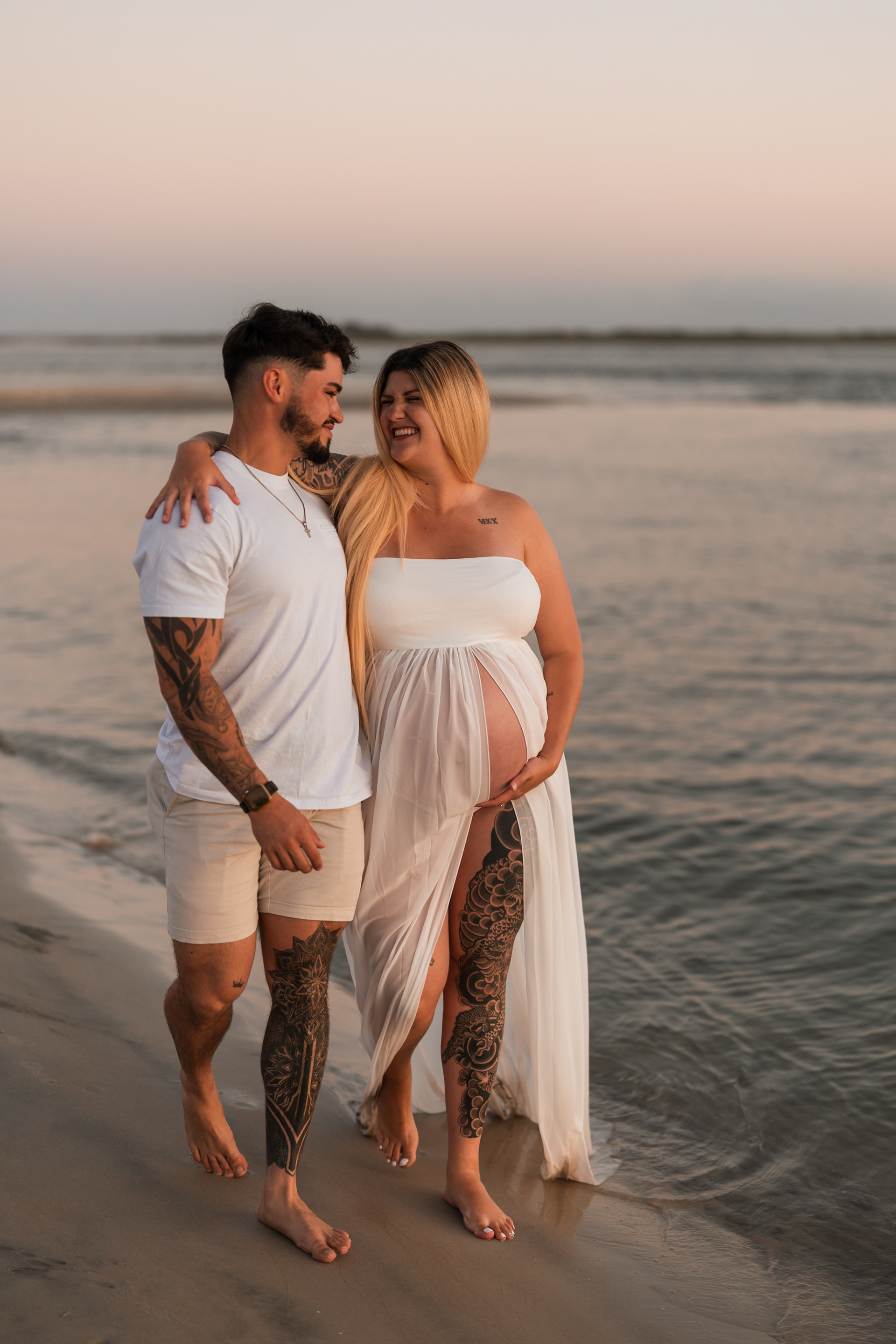Beach maternity portrait of expecting parents standing together in the water