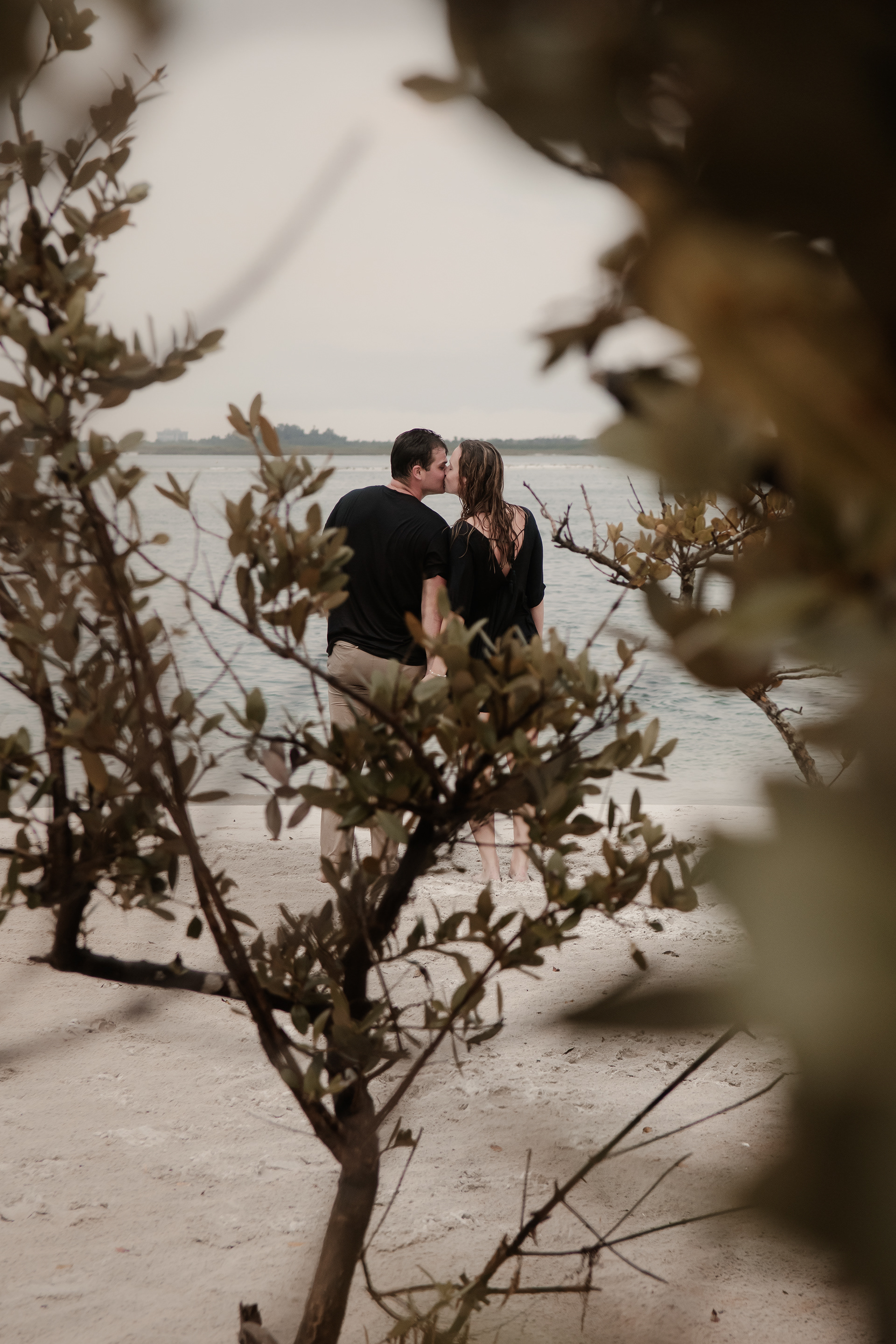 Candid Ponce Inlet engagement photo of couple kissing through beach greenery