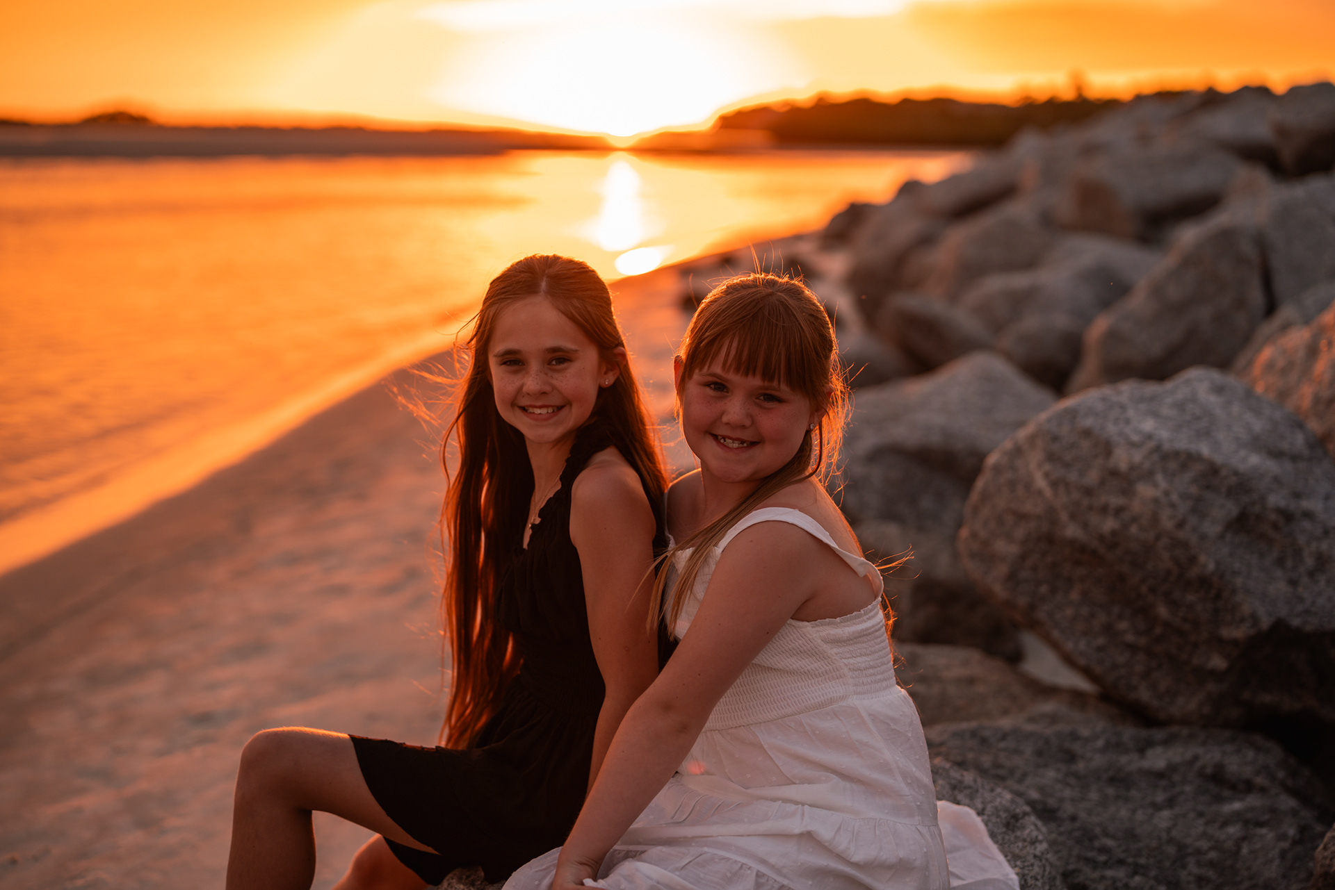 Sisters smiling near the rocks and shoreline during a Ponce Inlet Beach family photo session.