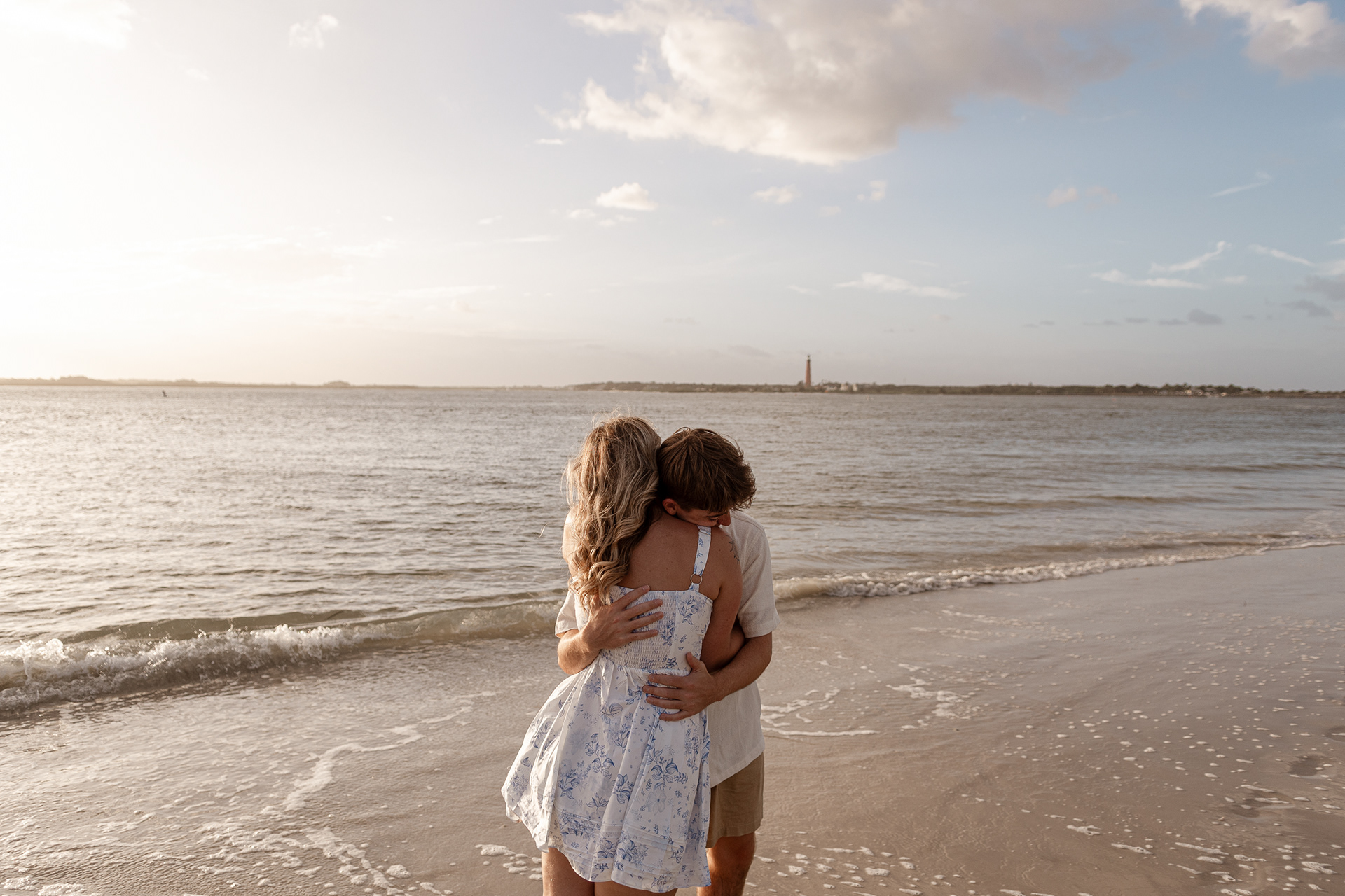 Couple hugging on the shoreline with the sun reflecting over the water at New Smyrna Beach.