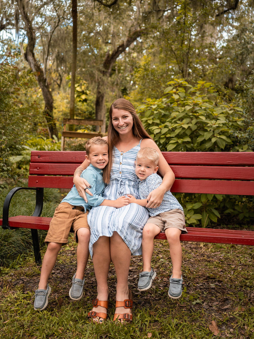 Mom sitting on a red bench holding her two youngest sons during family portraits in Port Orange, Florida.