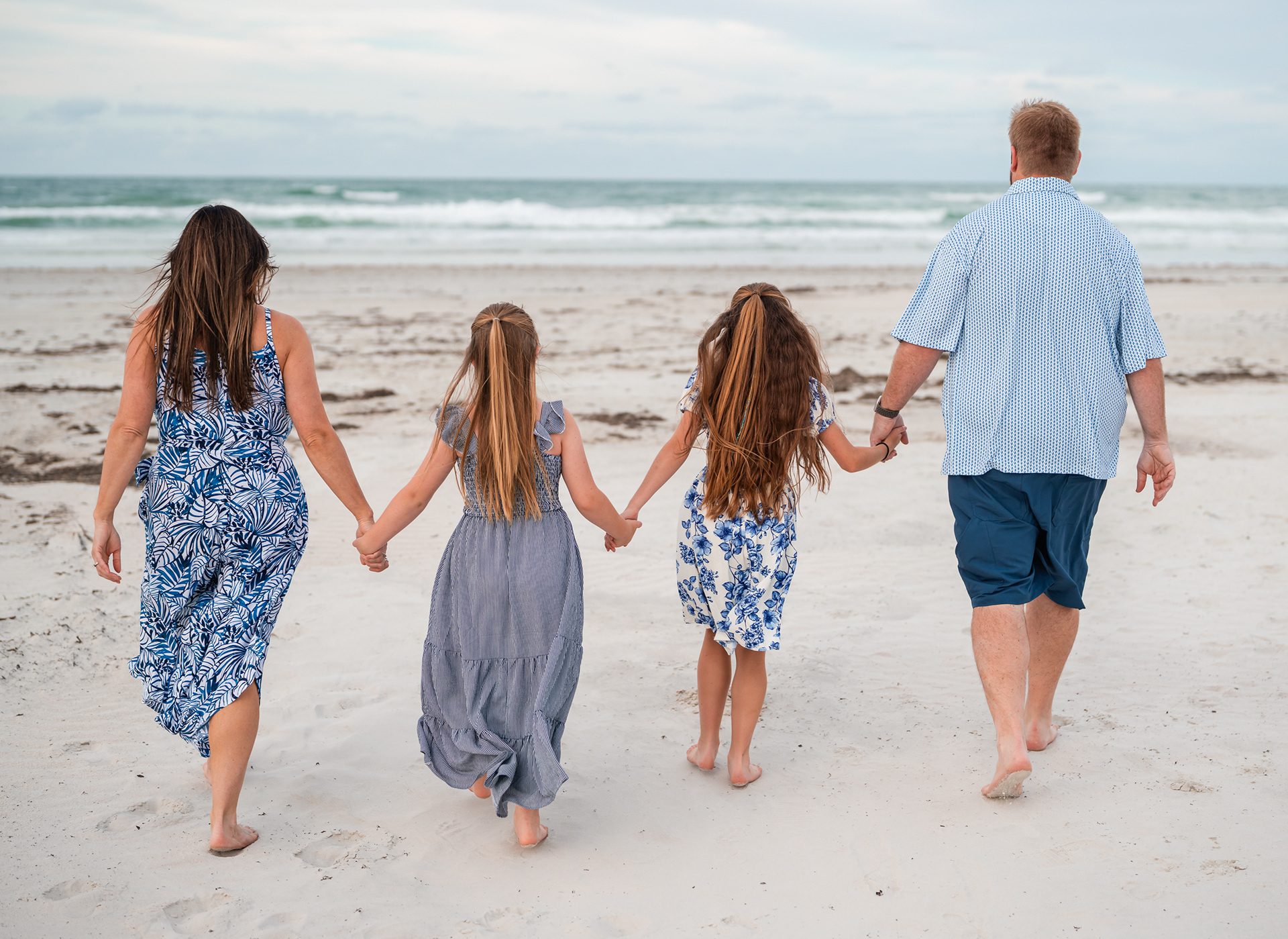 Family walking hand in hand on the sand during a Ponce Inlet Beach family photo session.