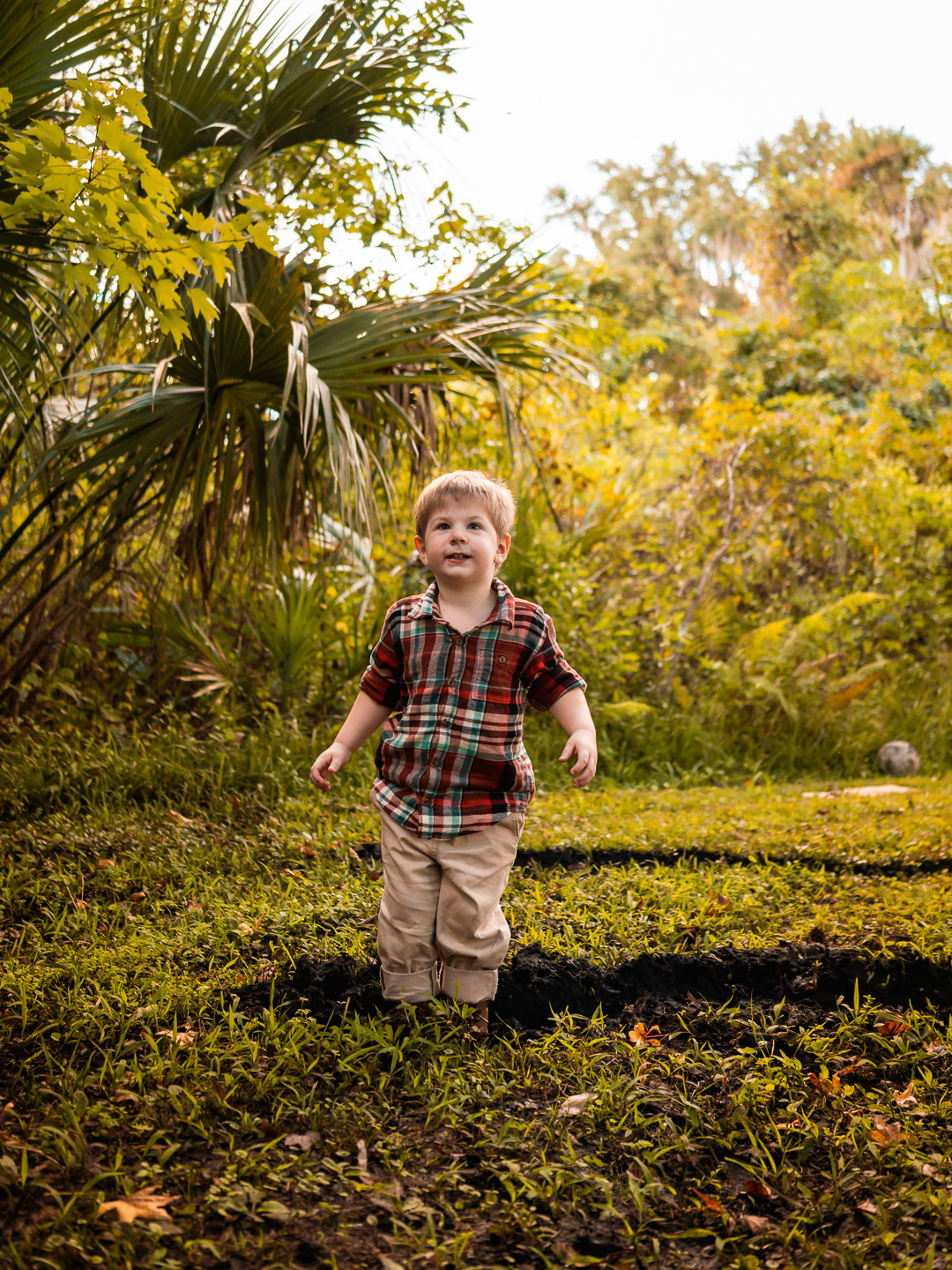 Candid photo of child walking through grass surrounded by trees during family photography in New Smyrna Beach.