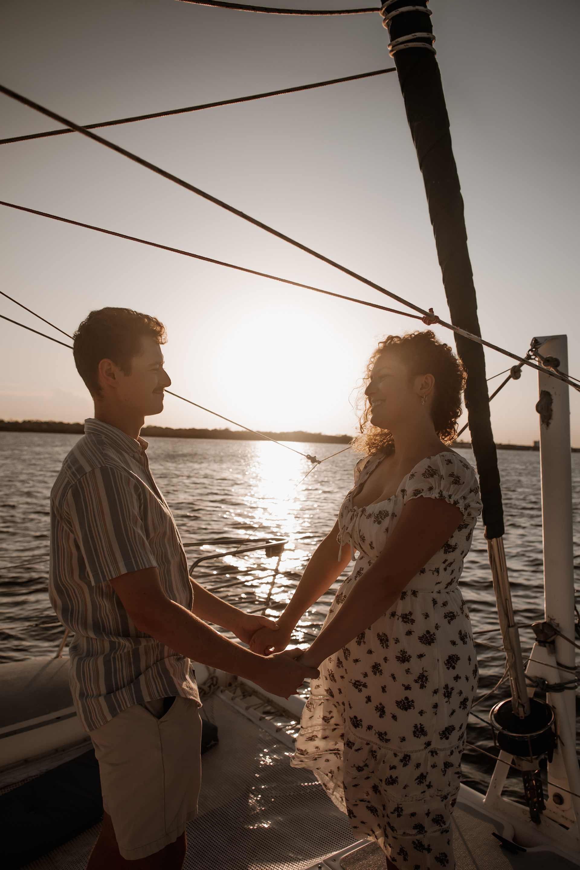 Silhouette engagement photo of couple holding hands on sailboat at sunset in Daytona Beach