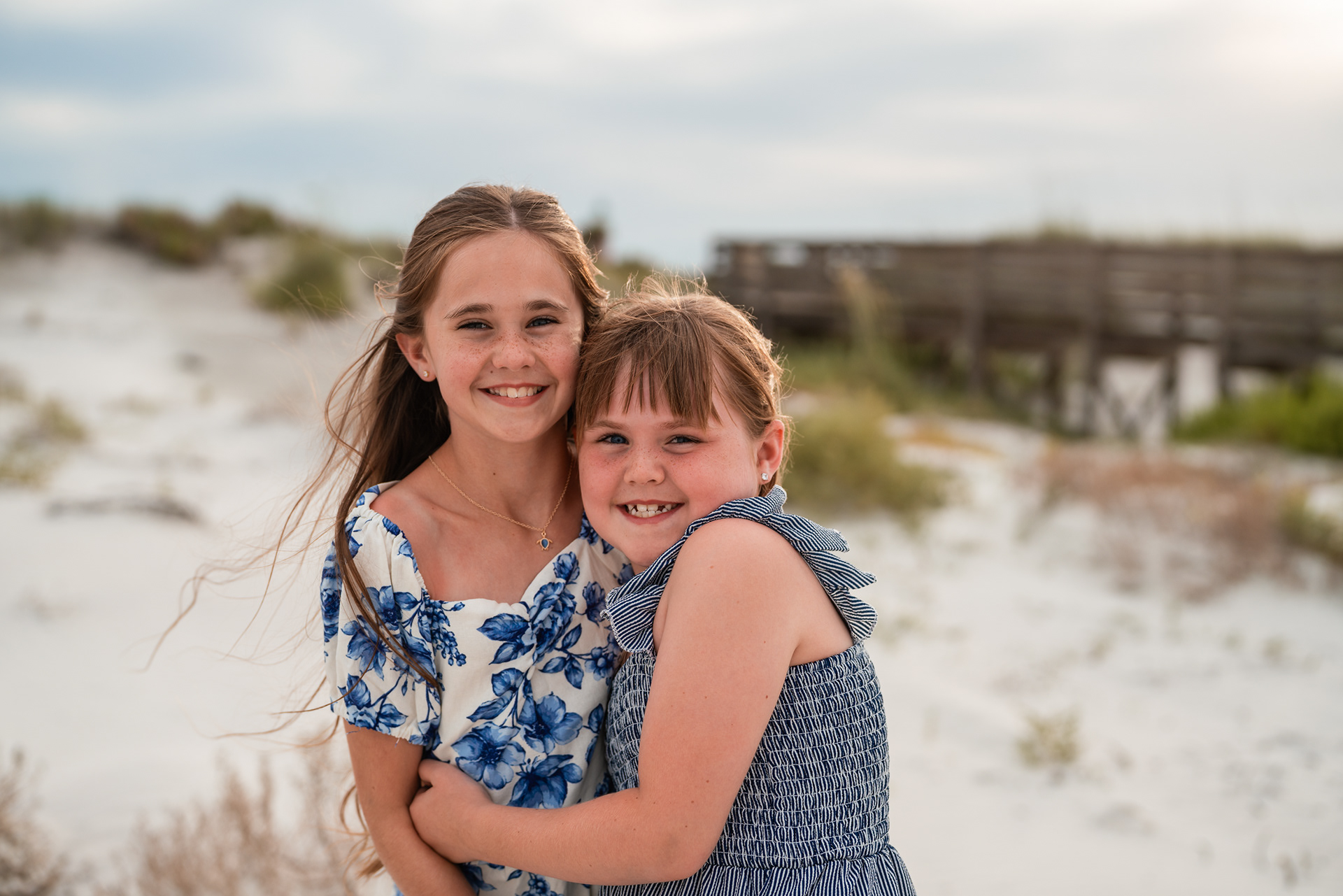 Sisters hugging in the dunes during a beach family photo session in Ponce Inlet.