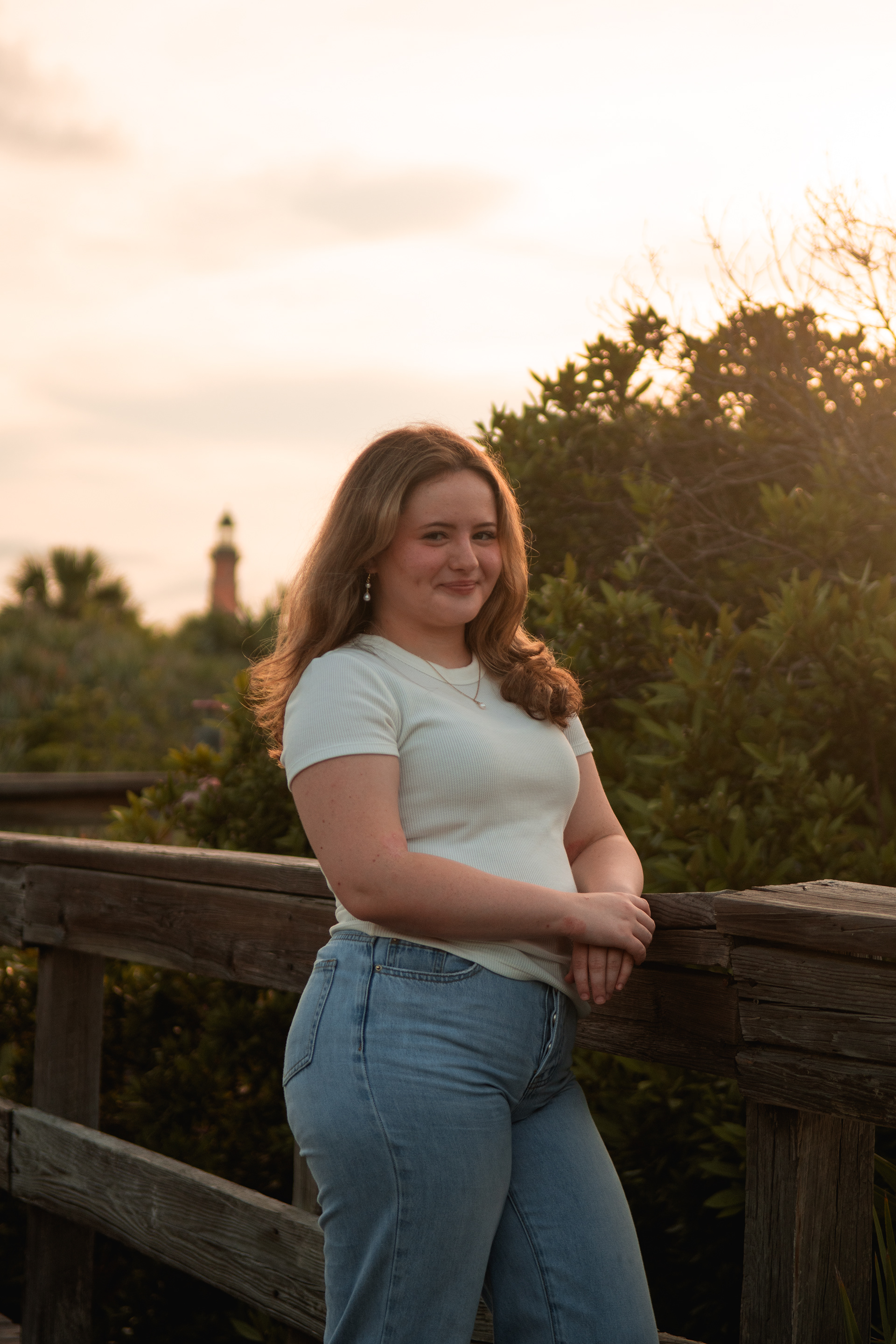 Senior photo at Ponce Inlet FL, Nelly smiling on the boardwalk in jeans and white top with sunset glow.
