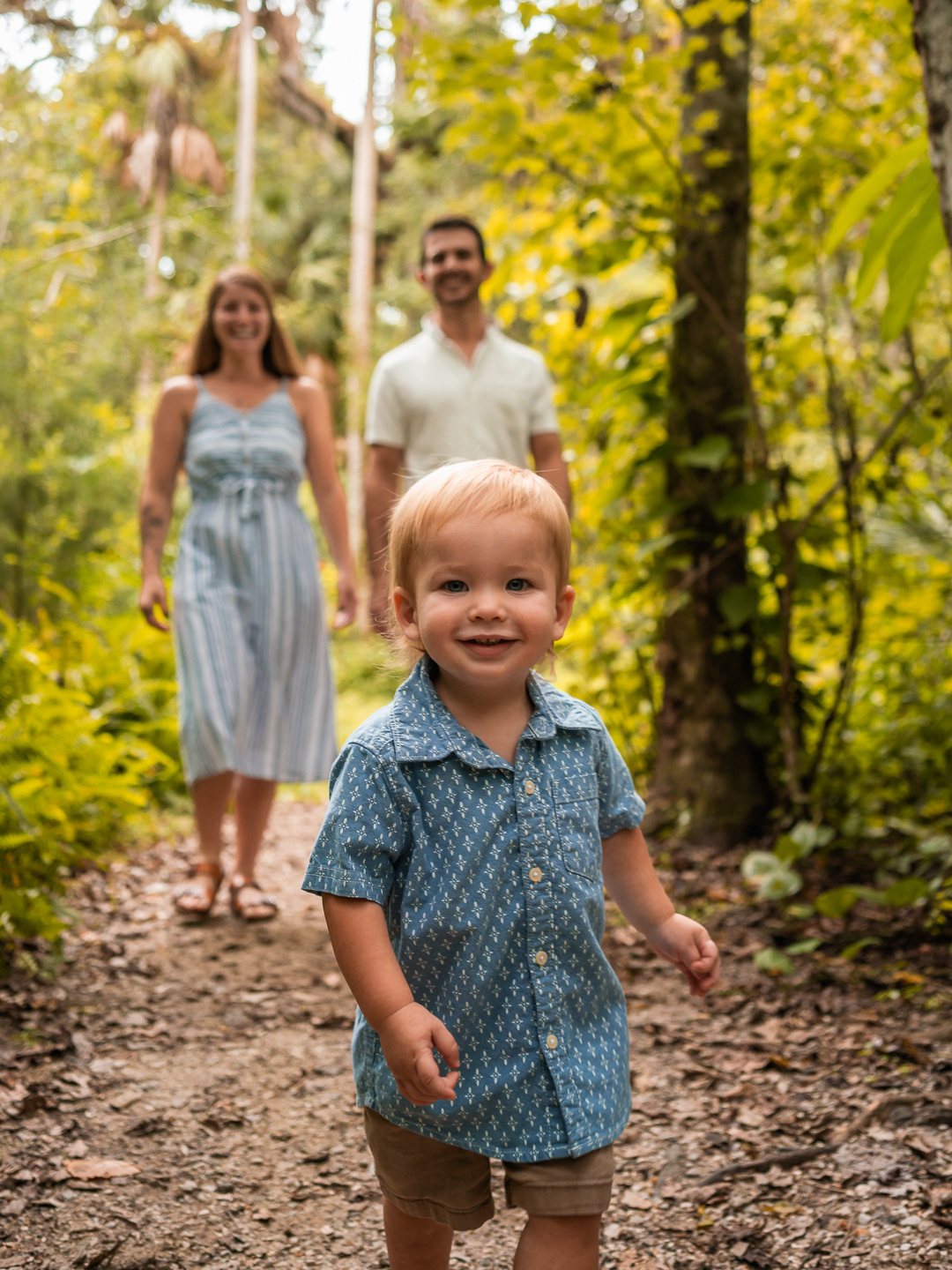 Young boy smiling and walking on a shaded trail while his family follows behind during a Port Orange family session.