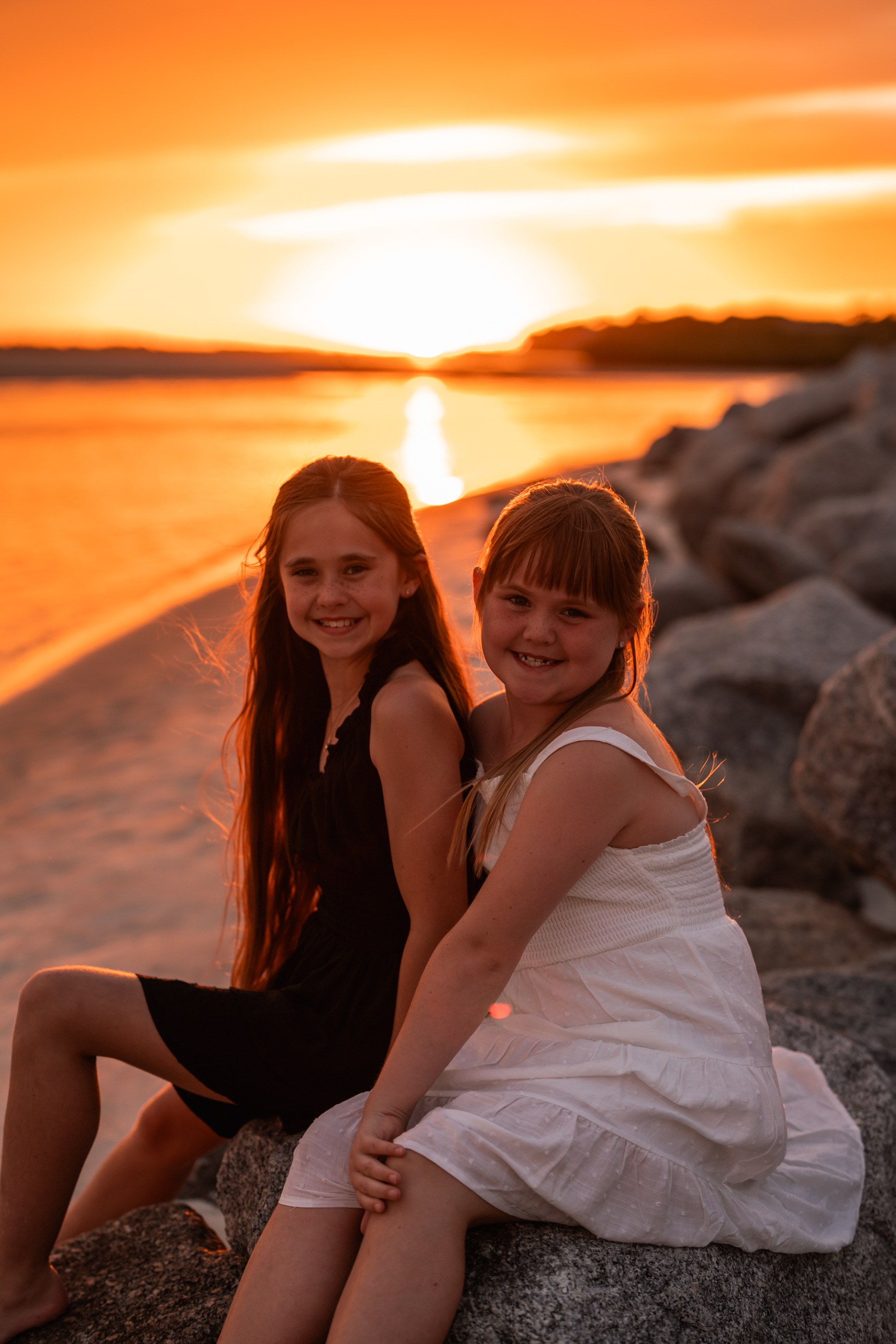 Two girls sitting together on the rocks during a family photography session at Ponce Inlet Beach.