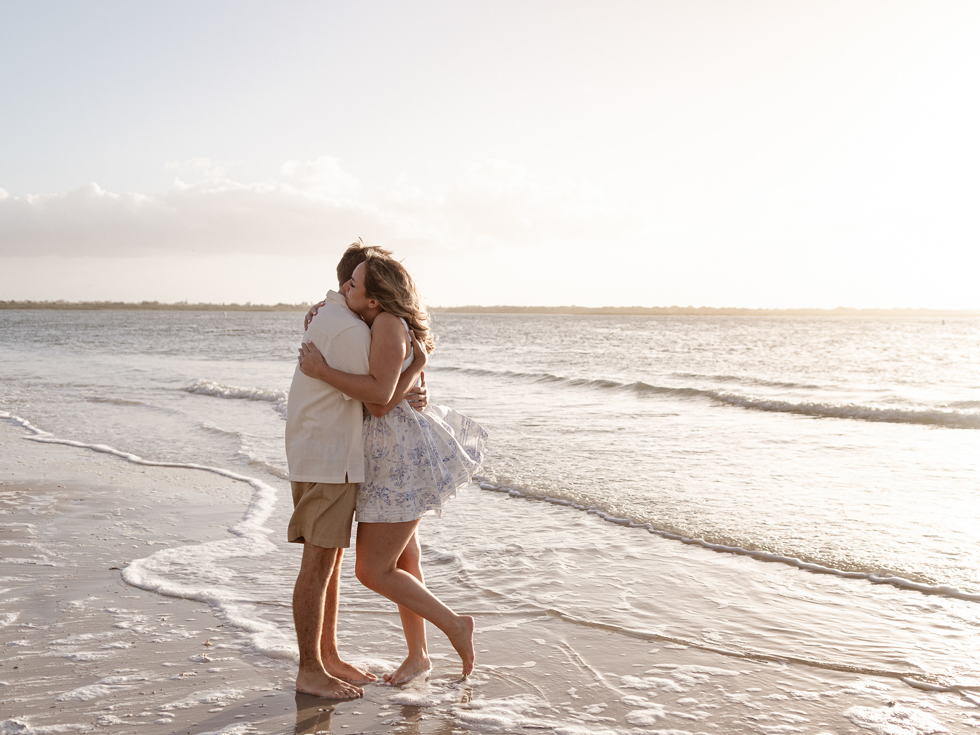Just-engaged couple kissing on the shoreline in New Smyrna Beach during golden evening light.
