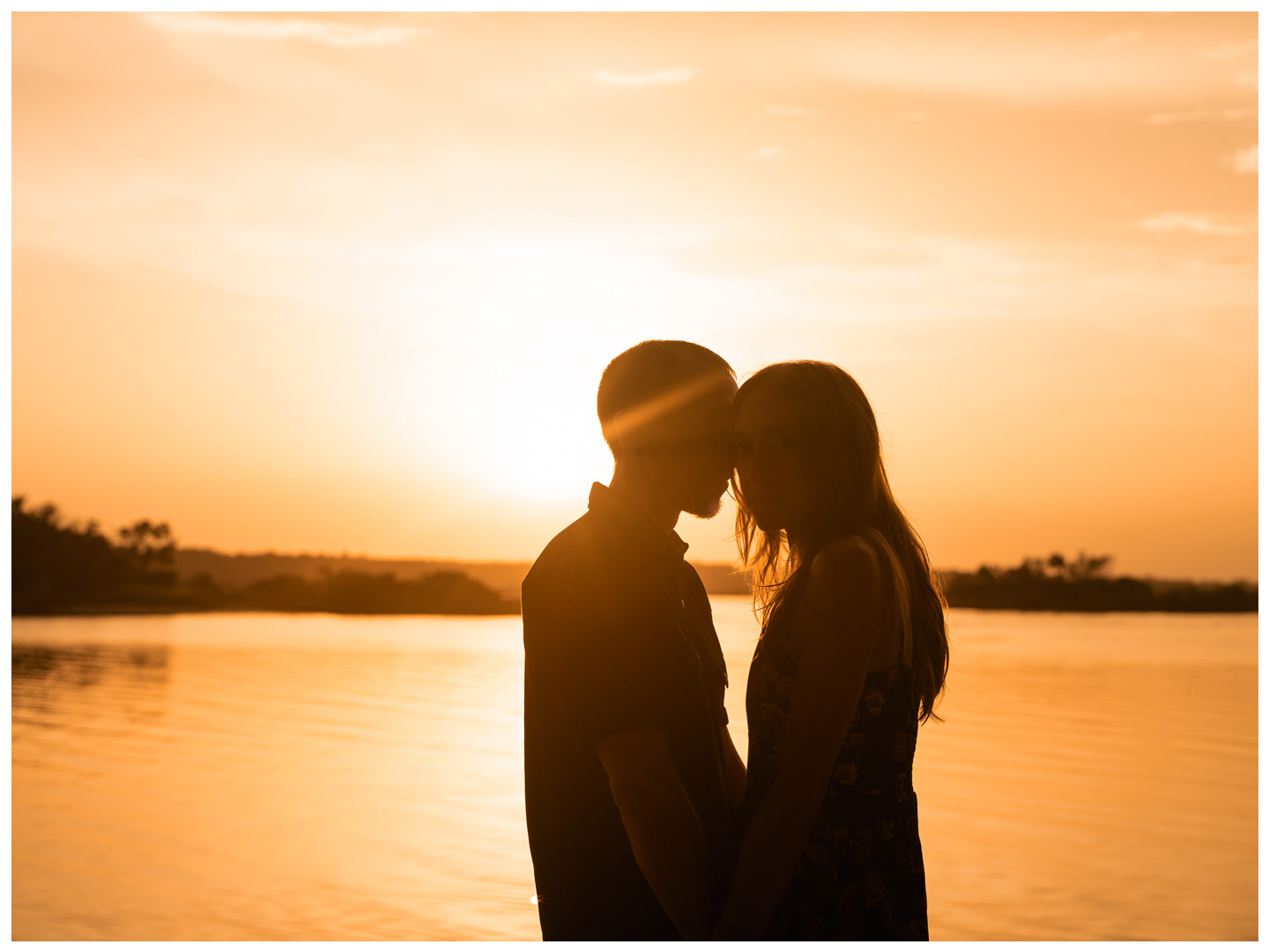 Silhouetted couple kissing against the sunset sky and river at Washington Oaks Gardens State Park.
