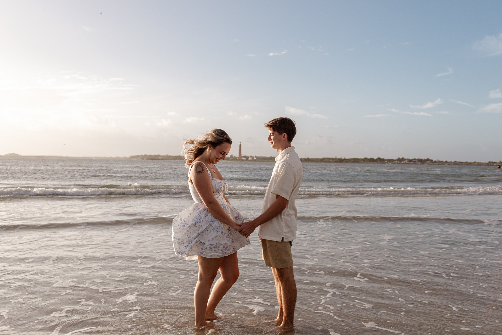 Engagement photos on the beach, Joey and Lexi smiling and holding hands in shallow ocean water.