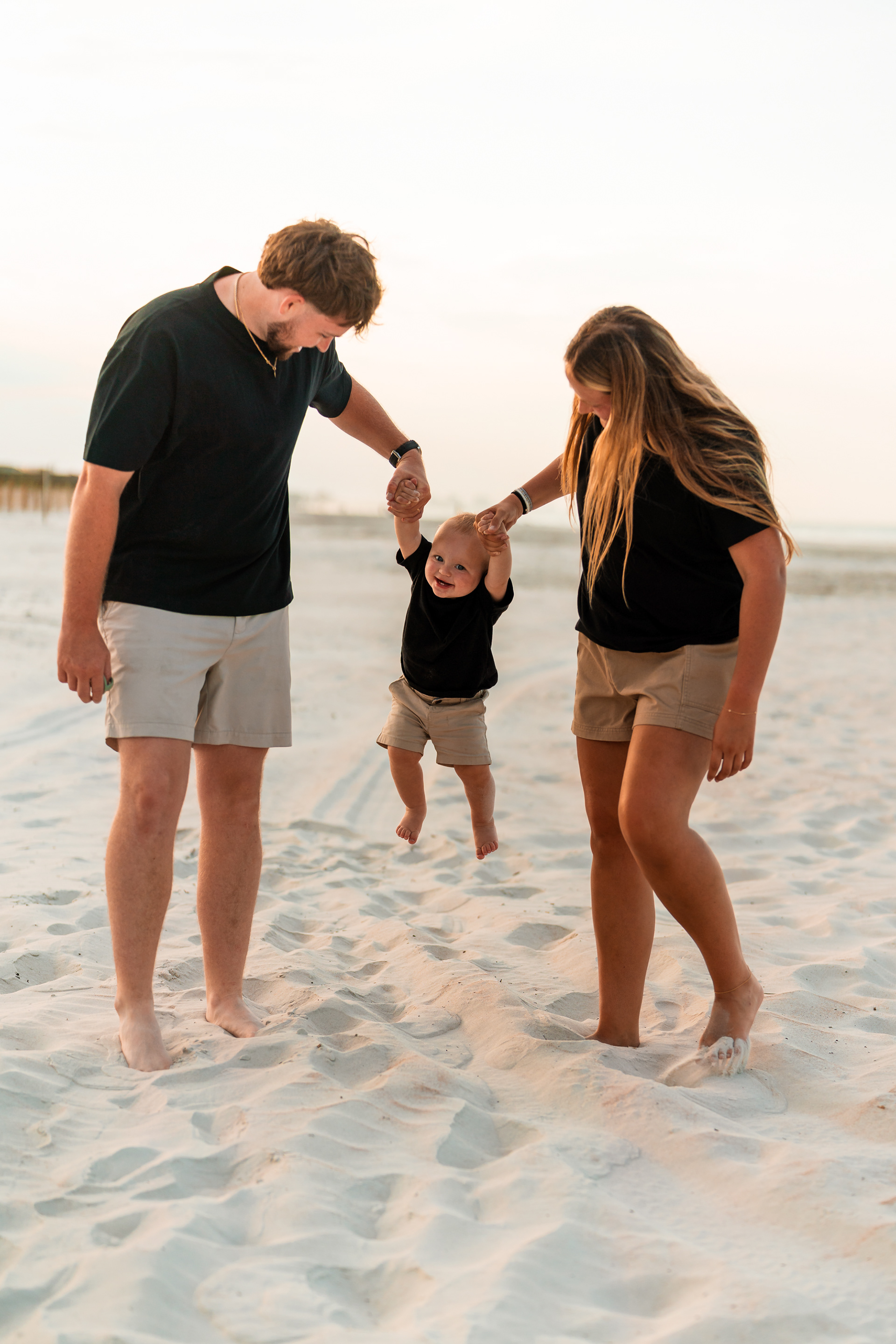 Parents holding their child’s hands while walking through the sand at Ponce Inlet Jetty Beach.