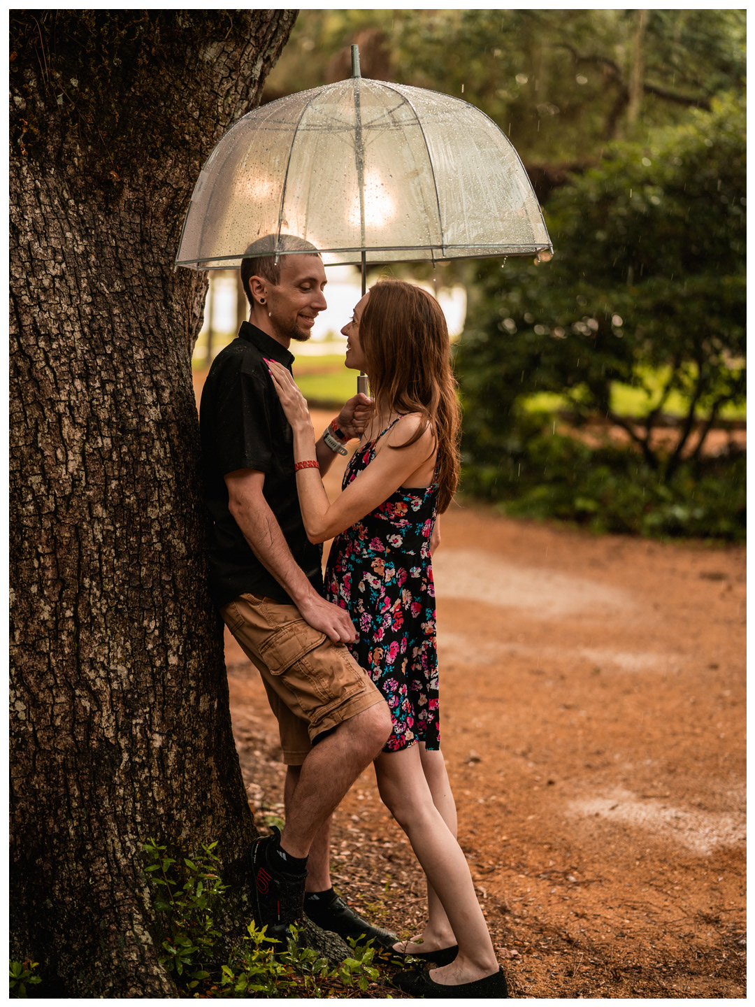 Couple embracing beside a large oak tree under a clear umbrella at Washington Oaks Gardens.