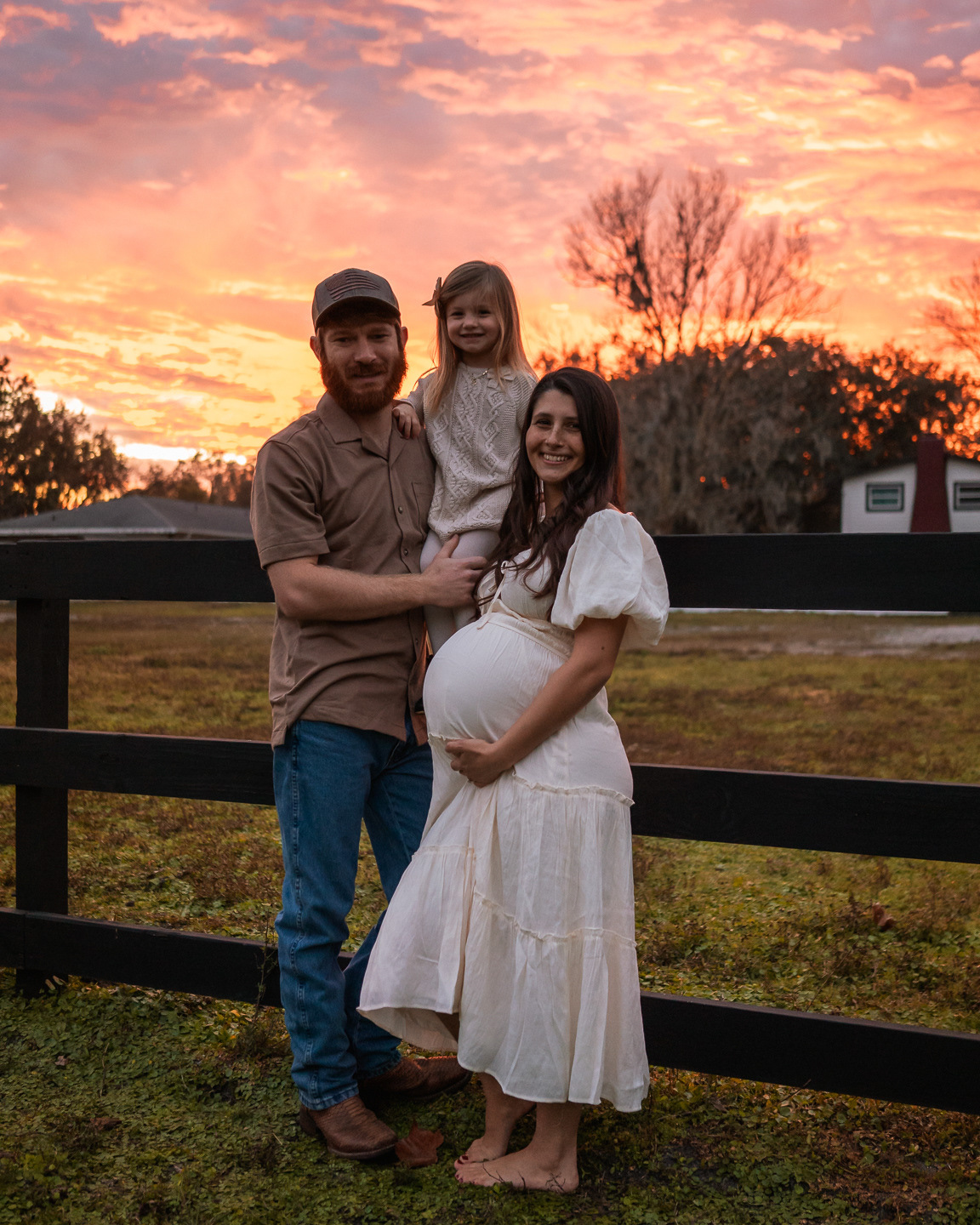 Sunset maternity photo of expecting couple standing together by a fence