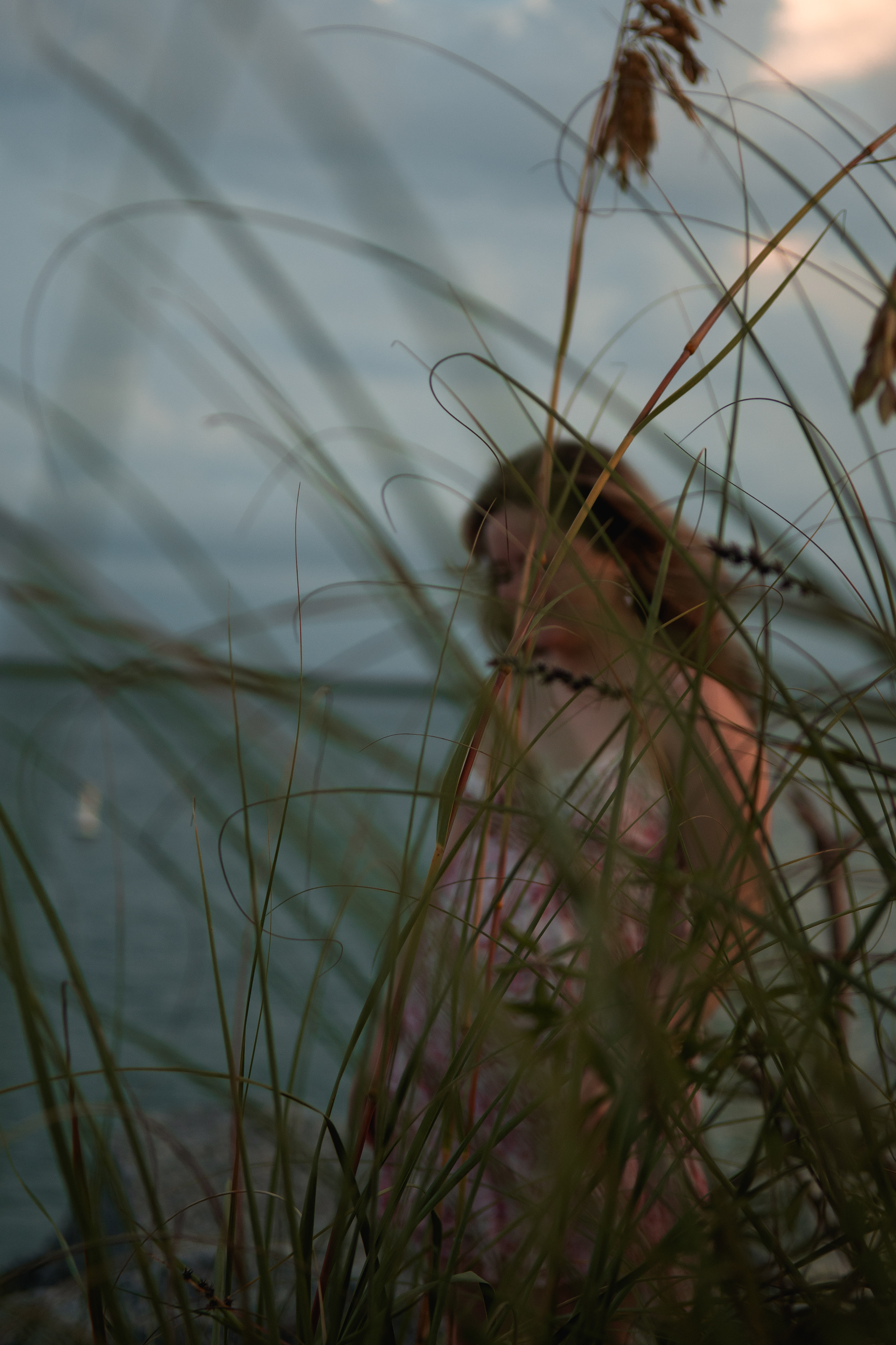 Close-up creative senior portrait in Ponce Inlet dunes with sea oats in focus, dreamy golden light.