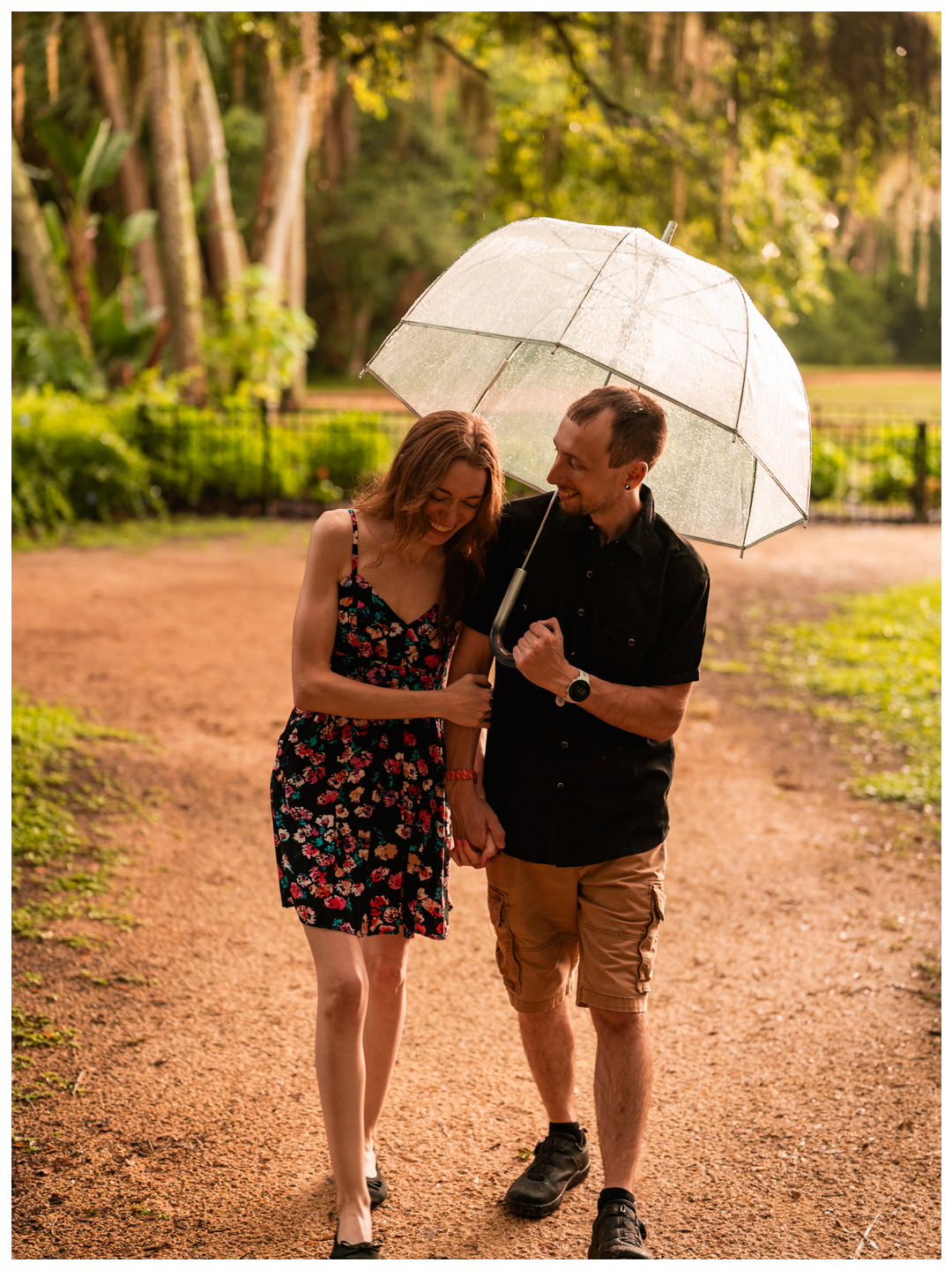 Couple walking together under a clear umbrella on a wet garden path at Washington Oaks.