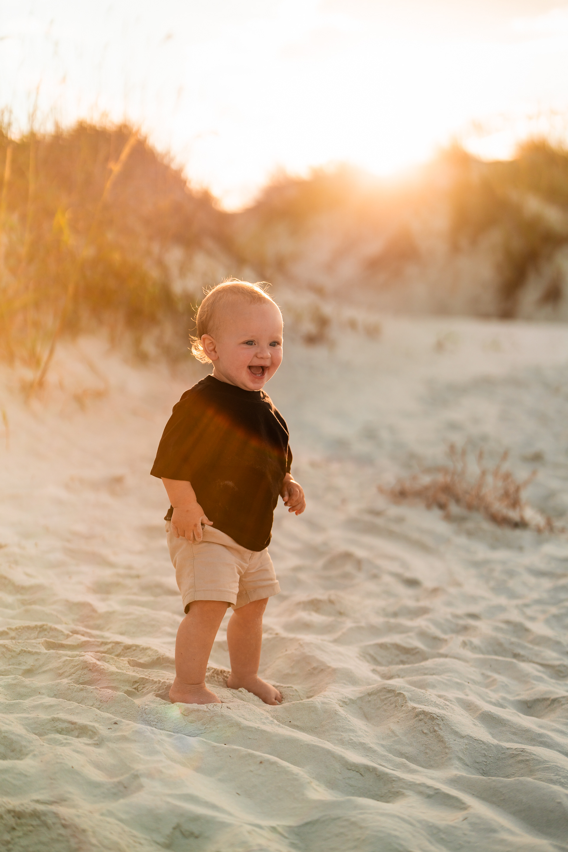 Toddler smiling in the sand during a sunset beach photo session at Ponce Inlet Jetty Beach.