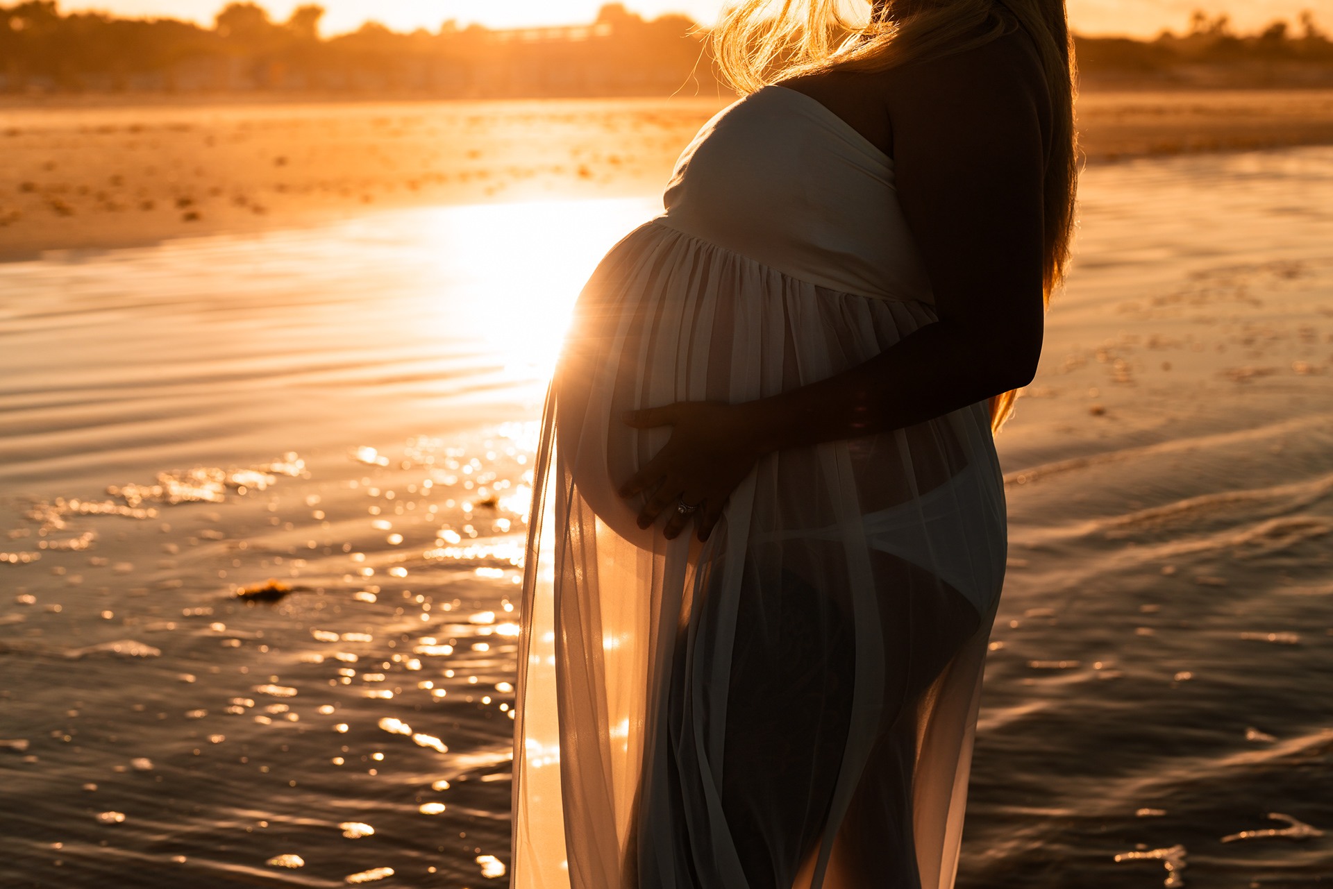 Close-up beach maternity photo of baby bump in warm sunset light