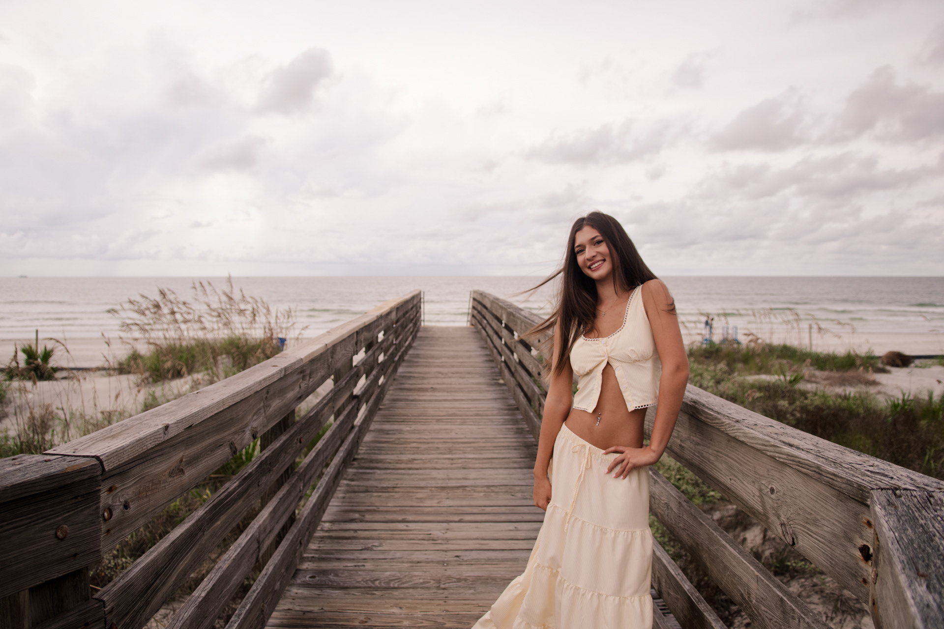 Senior photos at Ponce Inlet Beach, Mia standing on the wooden boardwalk in cream dress with ocean view behind her.