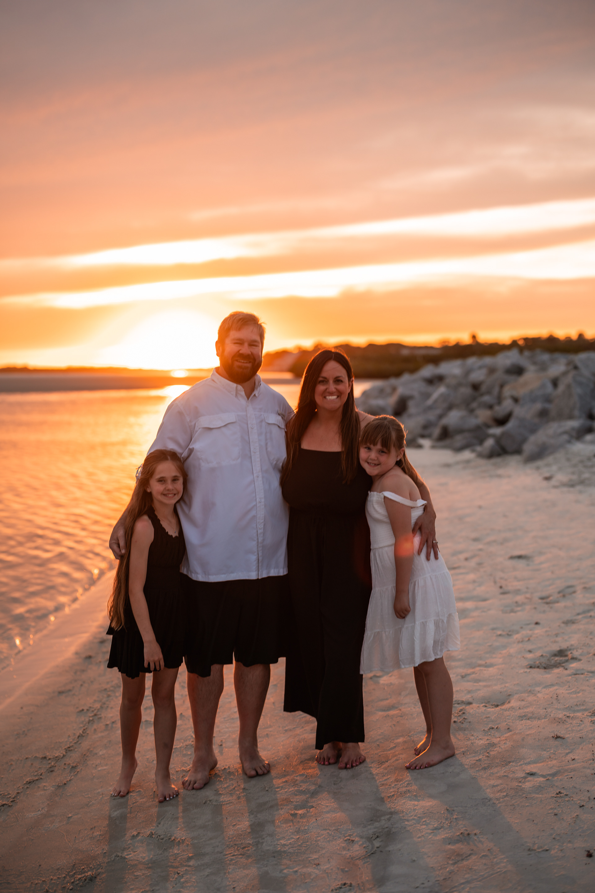 Family portrait near the rocks and shoreline during a sunset beach session in Ponce Inlet.