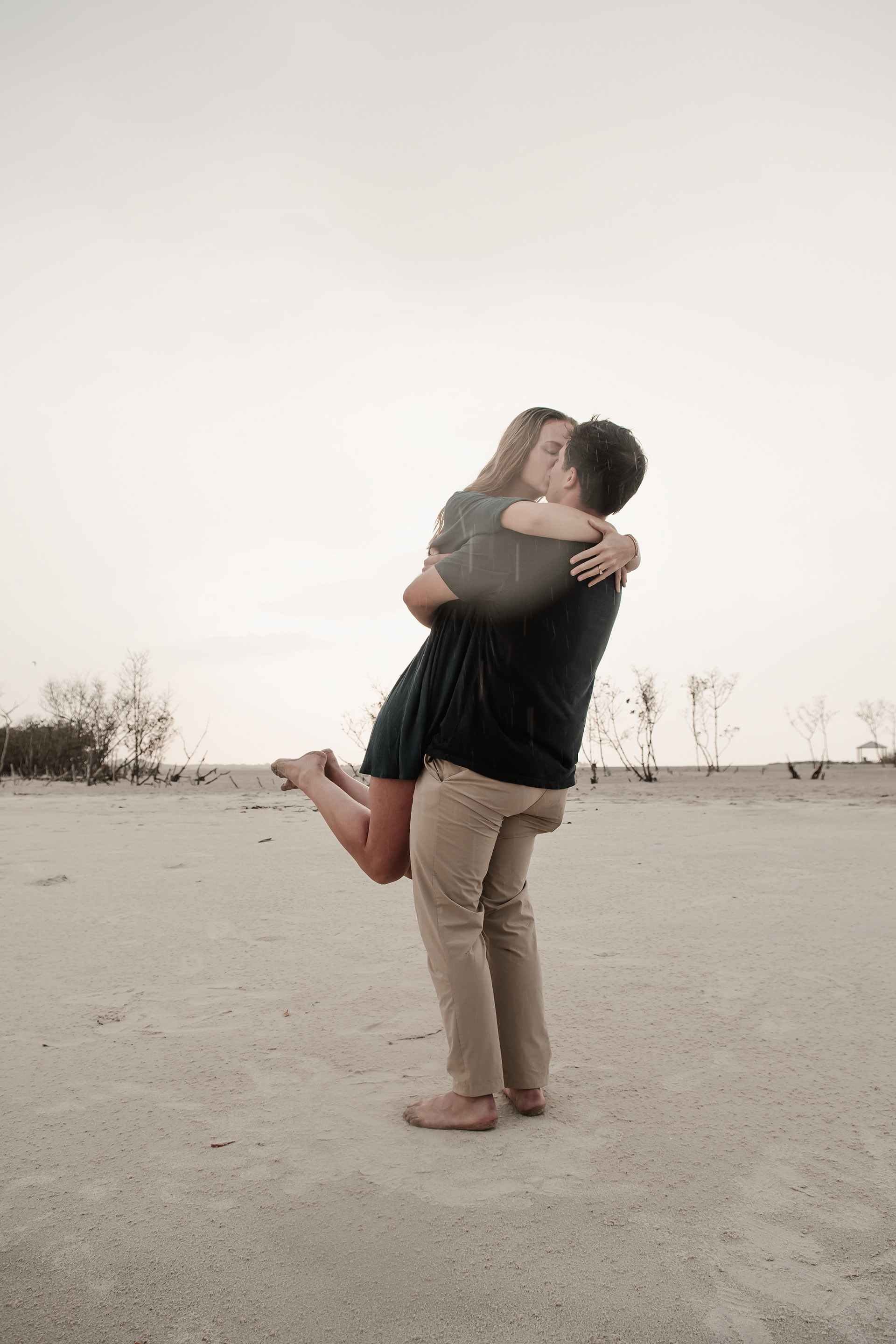 Rainy beach engagement photo of groom lifting bride-to-be at Ponce Inlet Florida