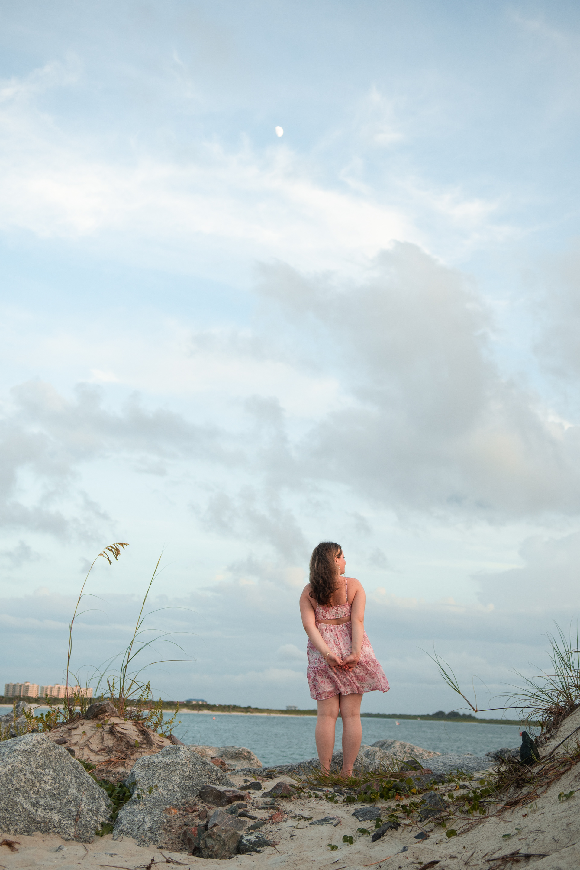 Senior portraits at the jetty in Ponce Inlet FL, Nelly standing in pink floral dress on the shoreline rocks.