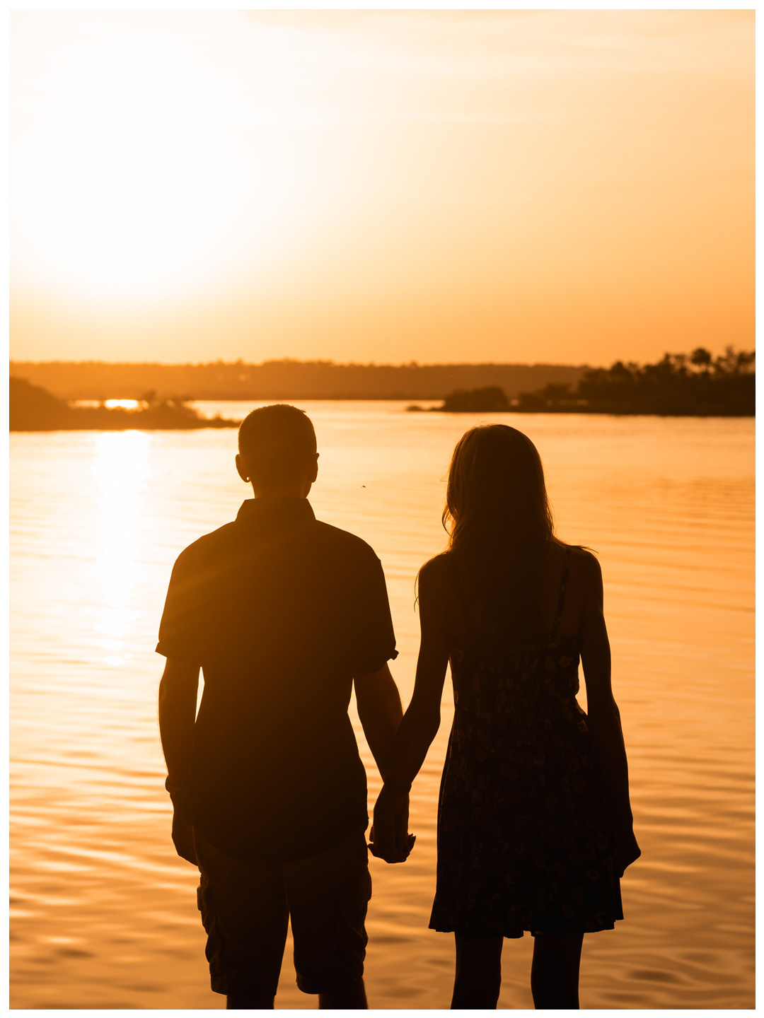 Couple holding hands in silhouette while facing the Matanzas River at sunset at Washington Oaks Gardens.