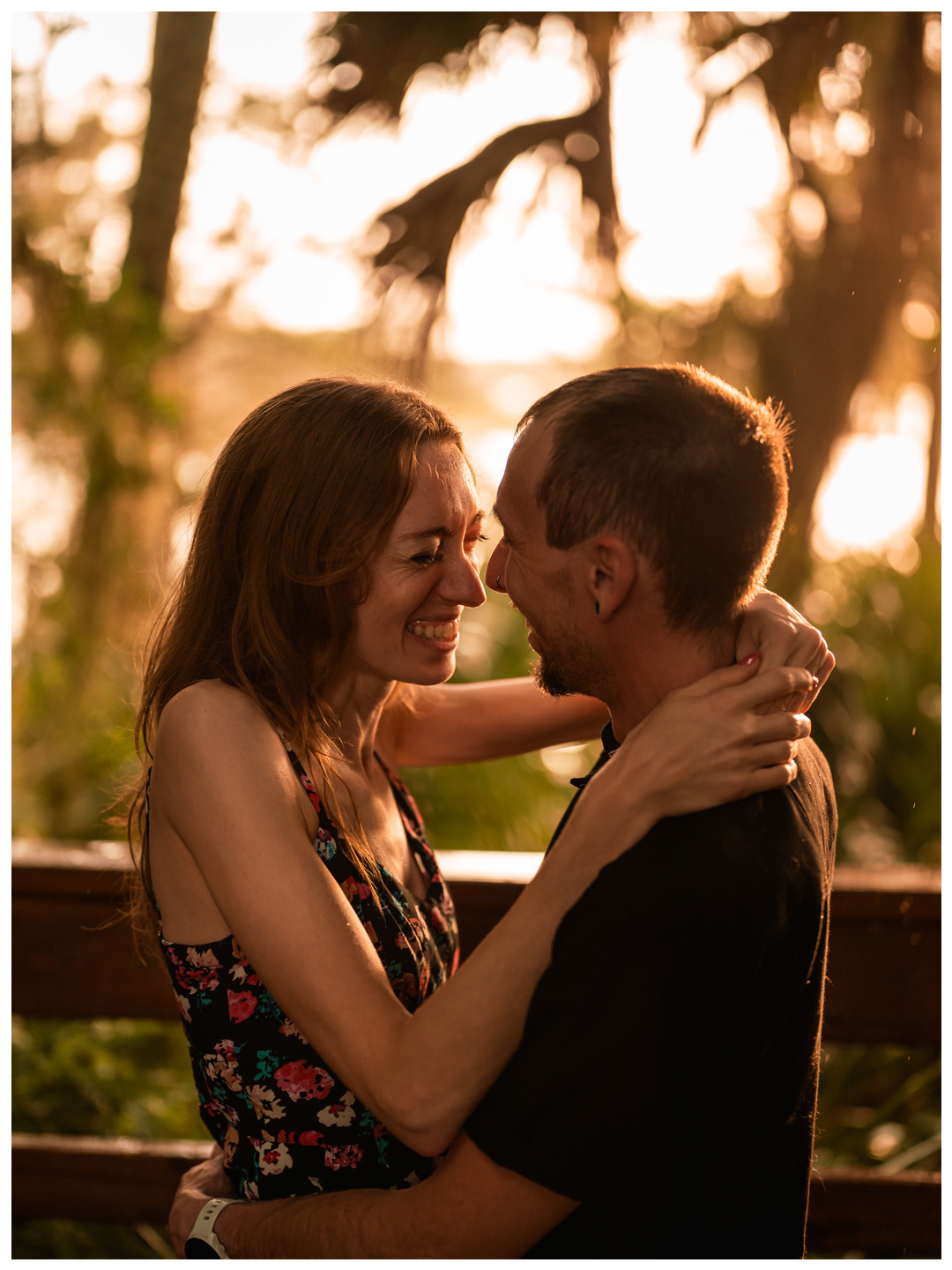 Close portrait of a couple smiling with their foreheads together beside a wooden railing at Washington Oaks.