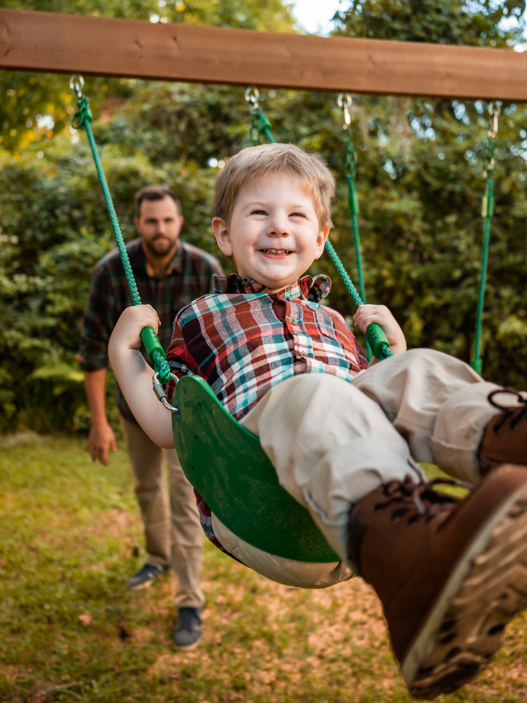 Little boy laughing on a swing while his dad pushes him during relaxed family photos in New Smyrna Beach.