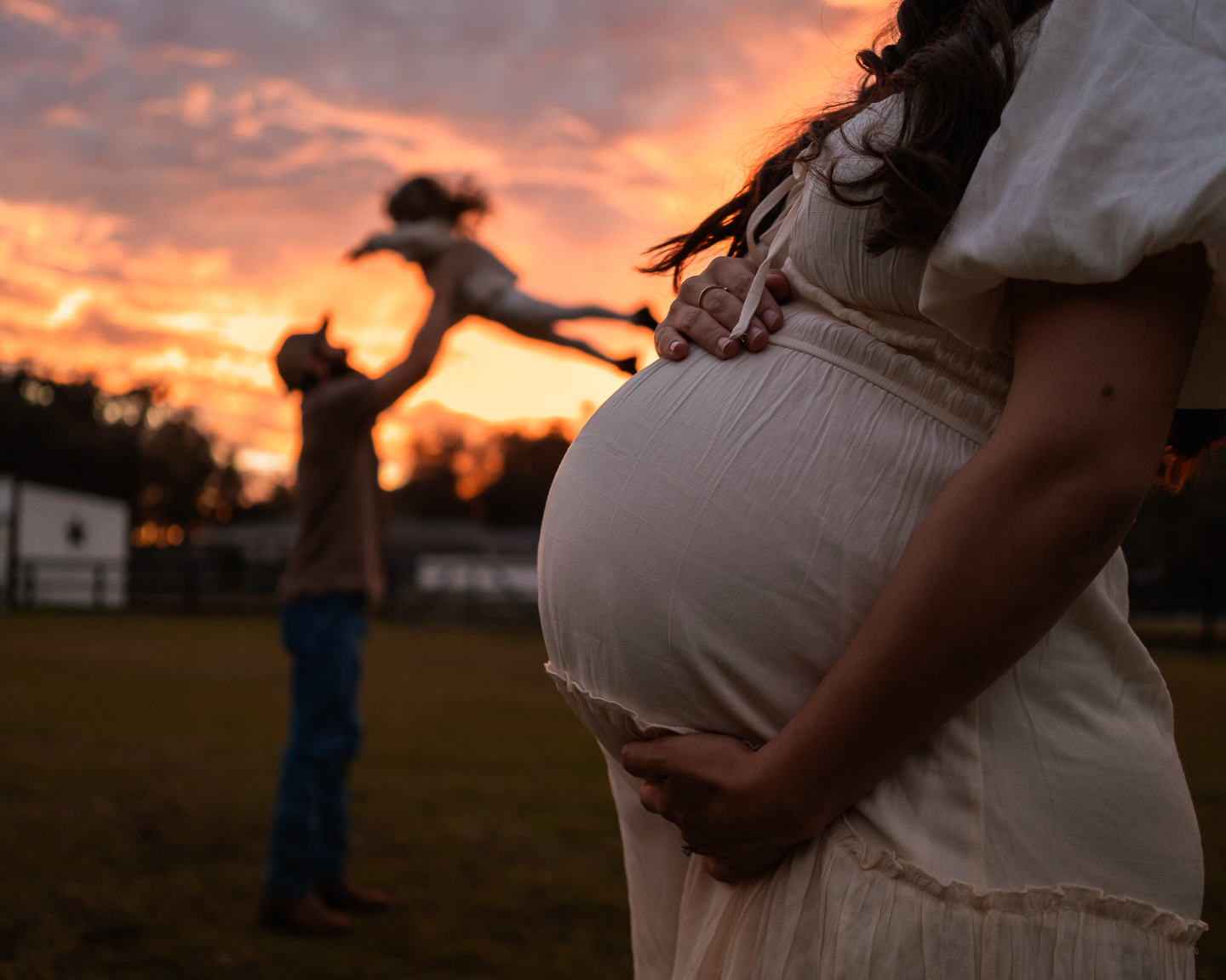 Outdoor maternity photo with pregnant mother holding baby bump at sunset