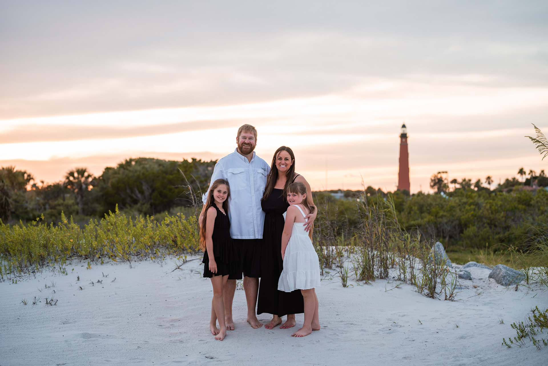 Family standing together on the sand with Ponce Inlet Lighthouse in the background.