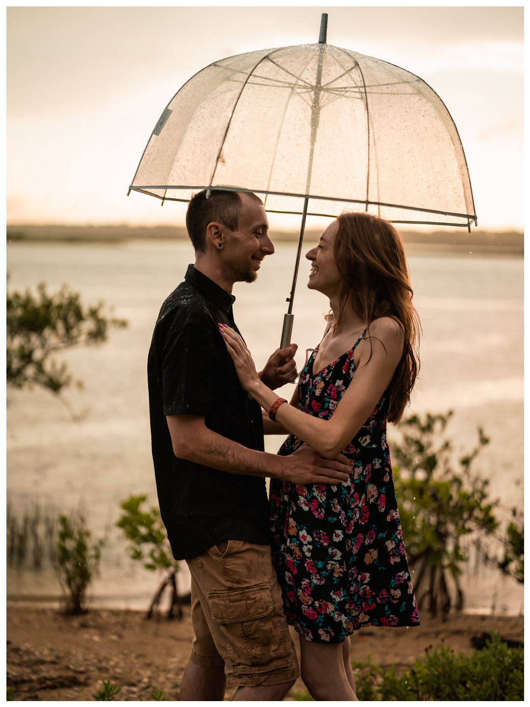 Couple facing each other beneath a clear umbrella near the Matanzas River at Washington Oaks Gardens.
