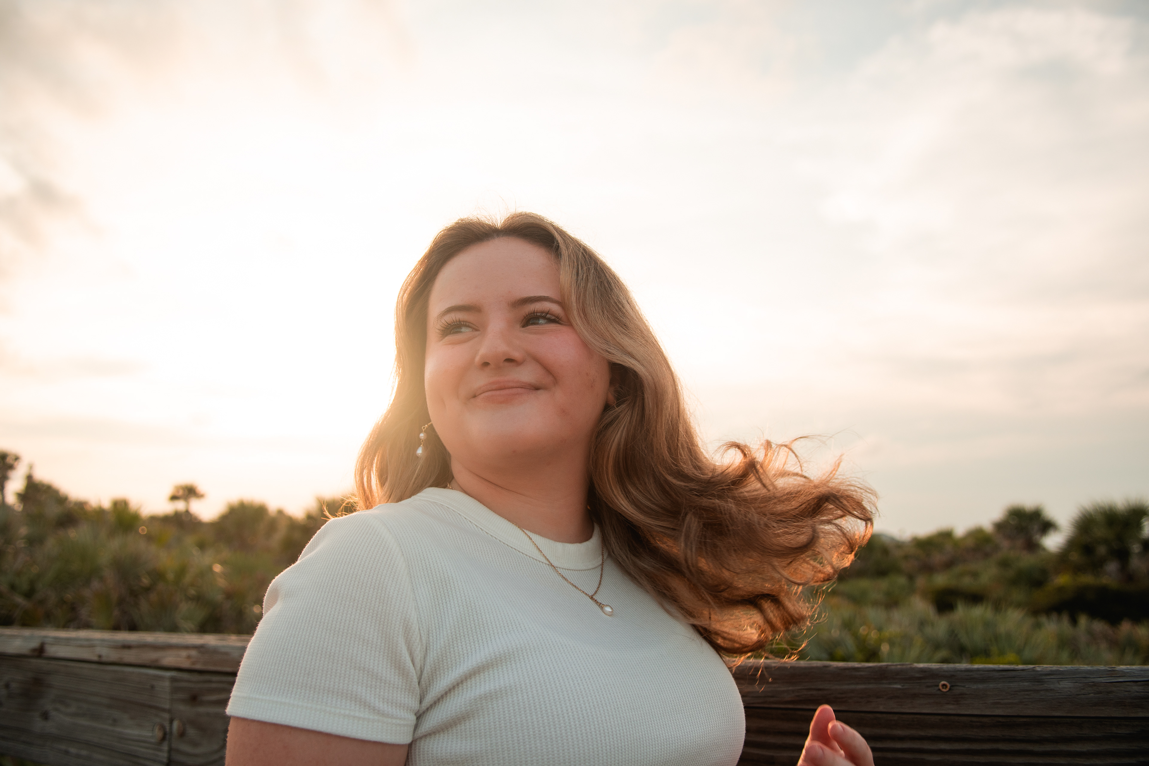 Senior portrait in Port Orange FL, Nelly smiling with golden backlight on her hair during sunset at Ponce Inlet.