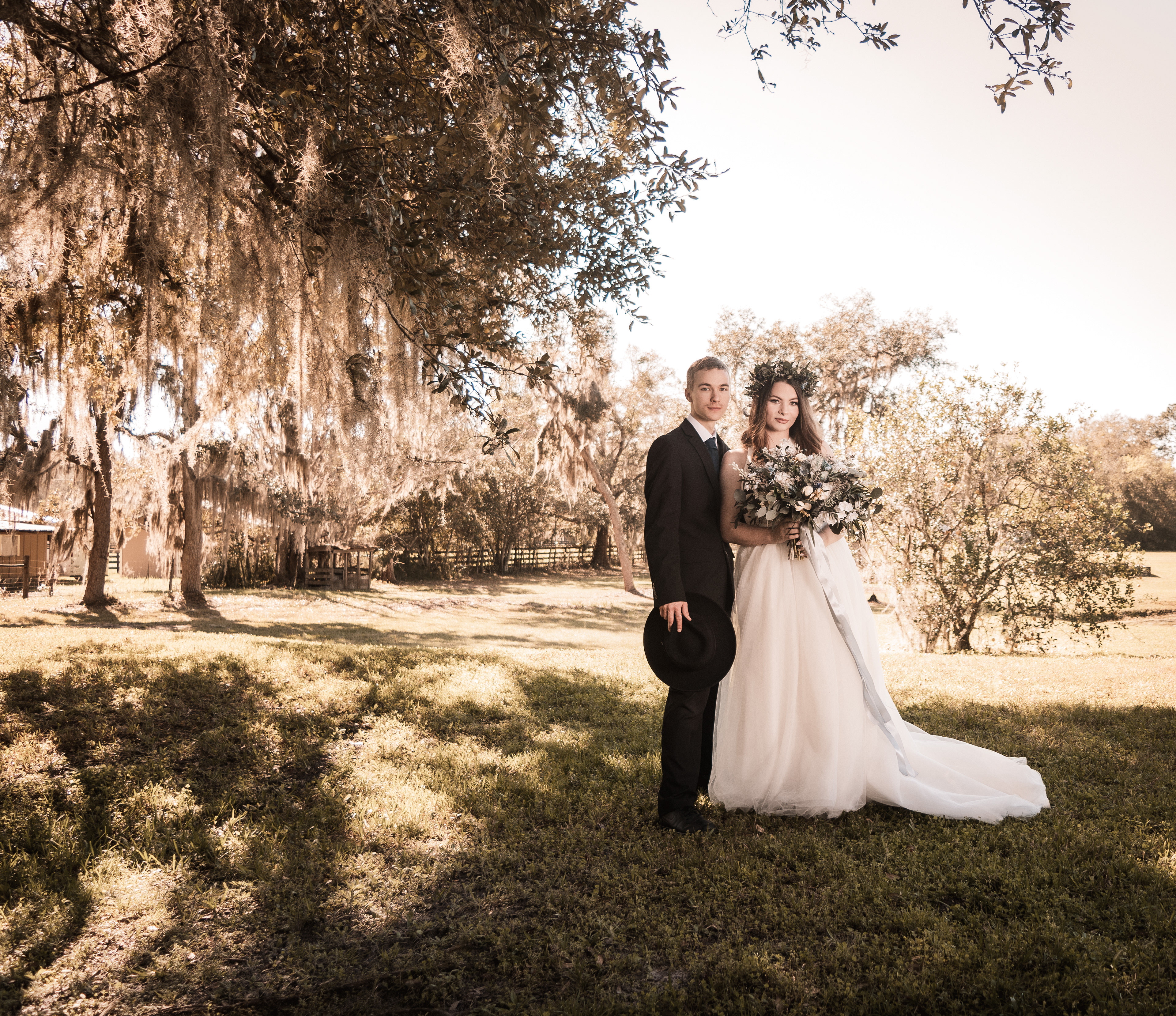 Outdoor wedding portraits under oak trees with Spanish moss, bride holding bouquet in lace gown and groom in black suit, Deland Florida wedding photography.