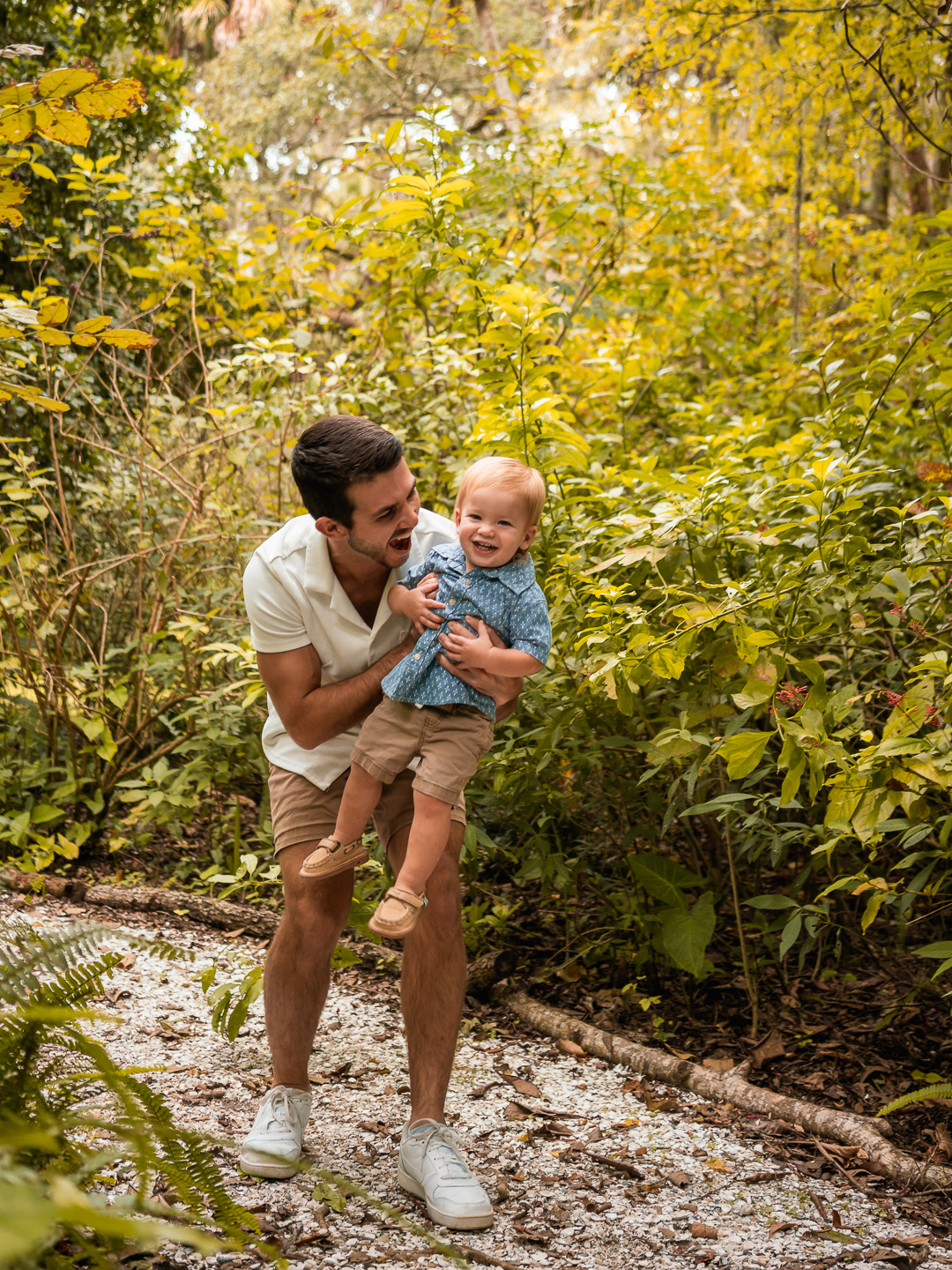 Father holding his young son while playing together on a shaded trail at Dunlawton Sugar Mill Gardens.