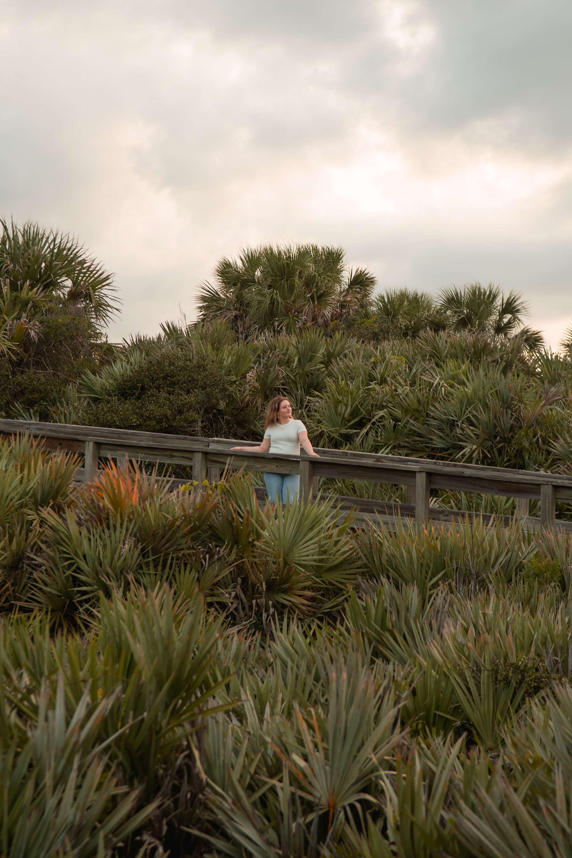 Senior portrait at Ponce Inlet, Nelly smiling while seated on dune with jeans and white shirt during golden hour.