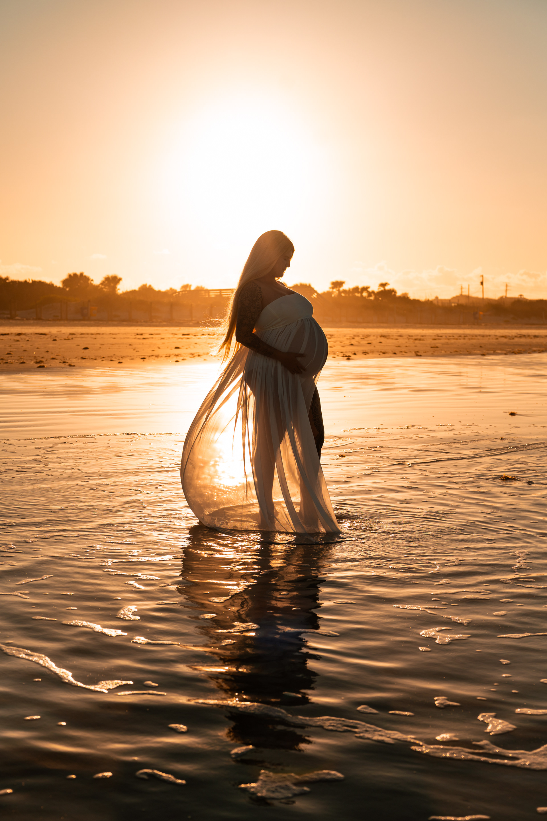 Silhouette maternity photo of pregnant mother standing in the water at sunset