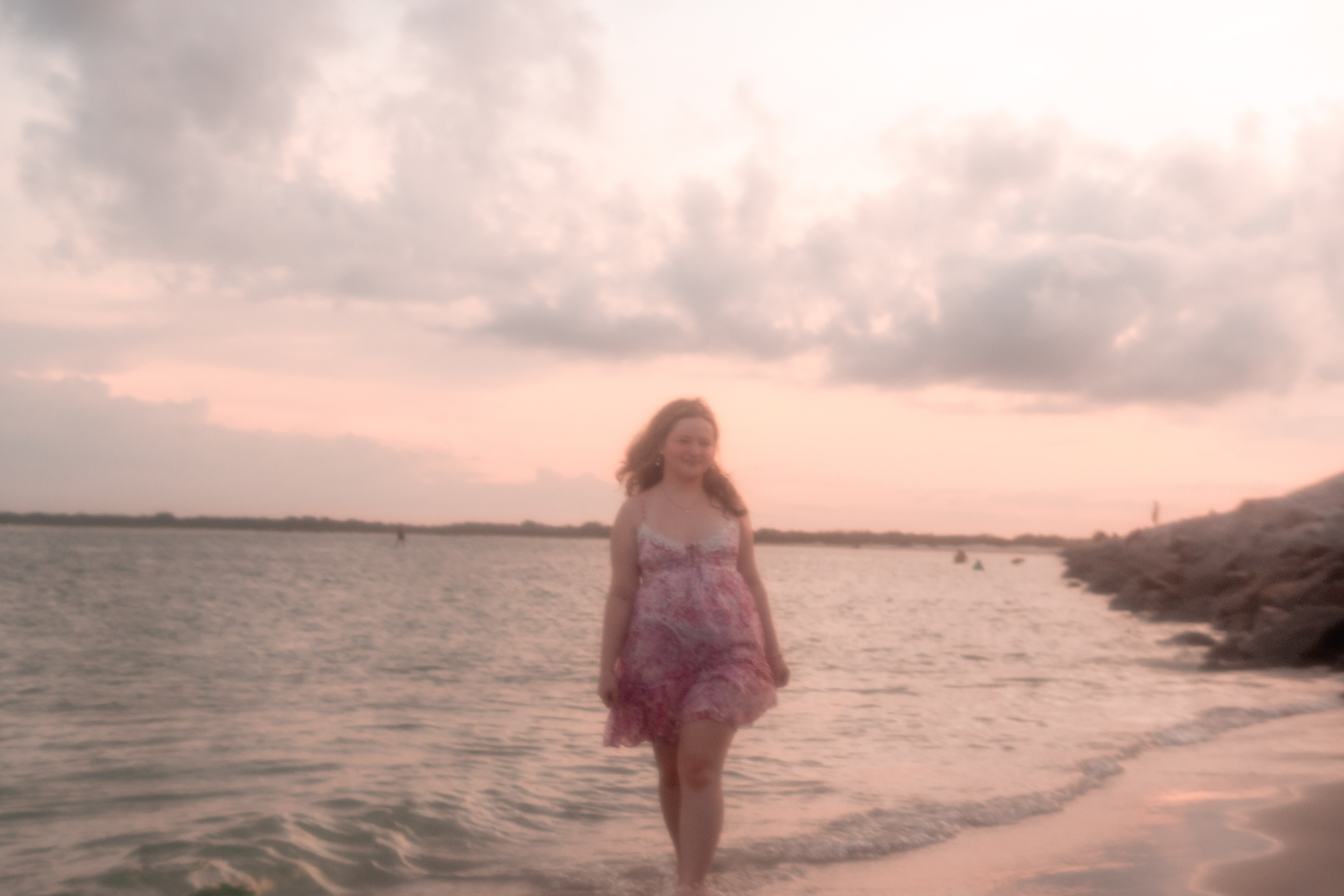 Senior portraits in Port Orange FL, Nelly walking in the water at sunset with pink sky reflections.