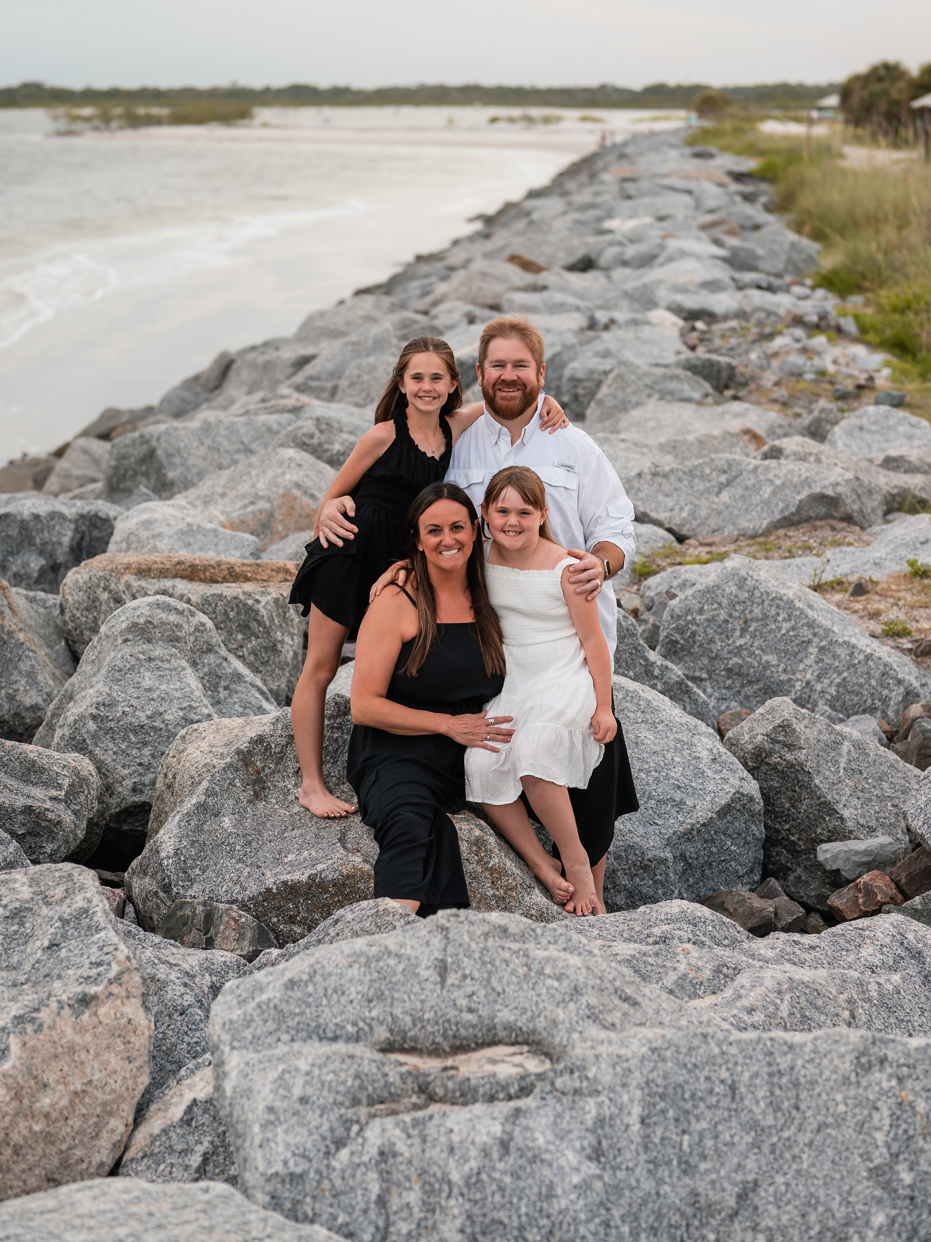 Family sitting together on the rocks during a Ponce Inlet Beach photo session.