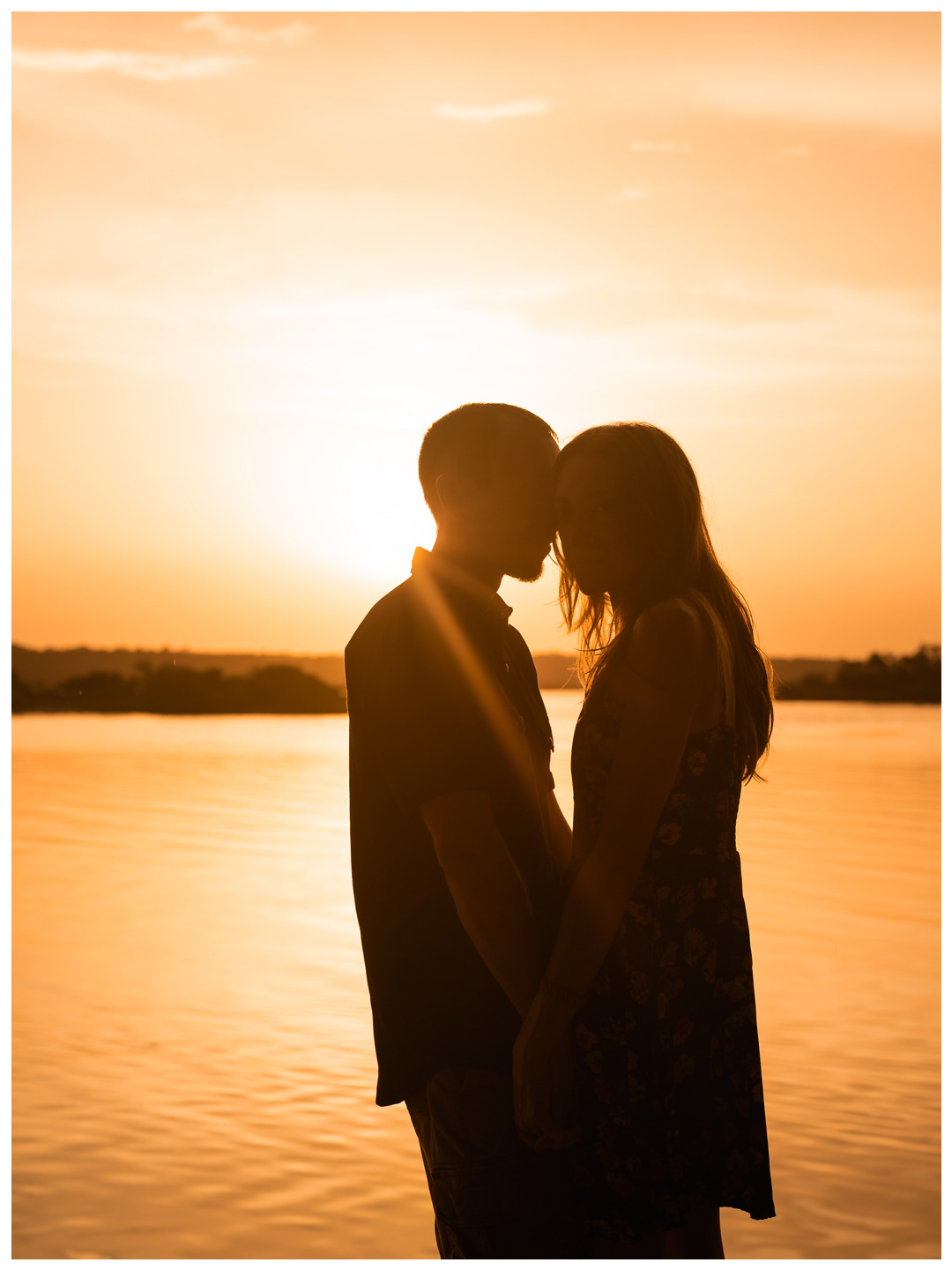 Vertical portrait of a couple kissing in silhouette along the waterfront at Washington Oaks Gardens.