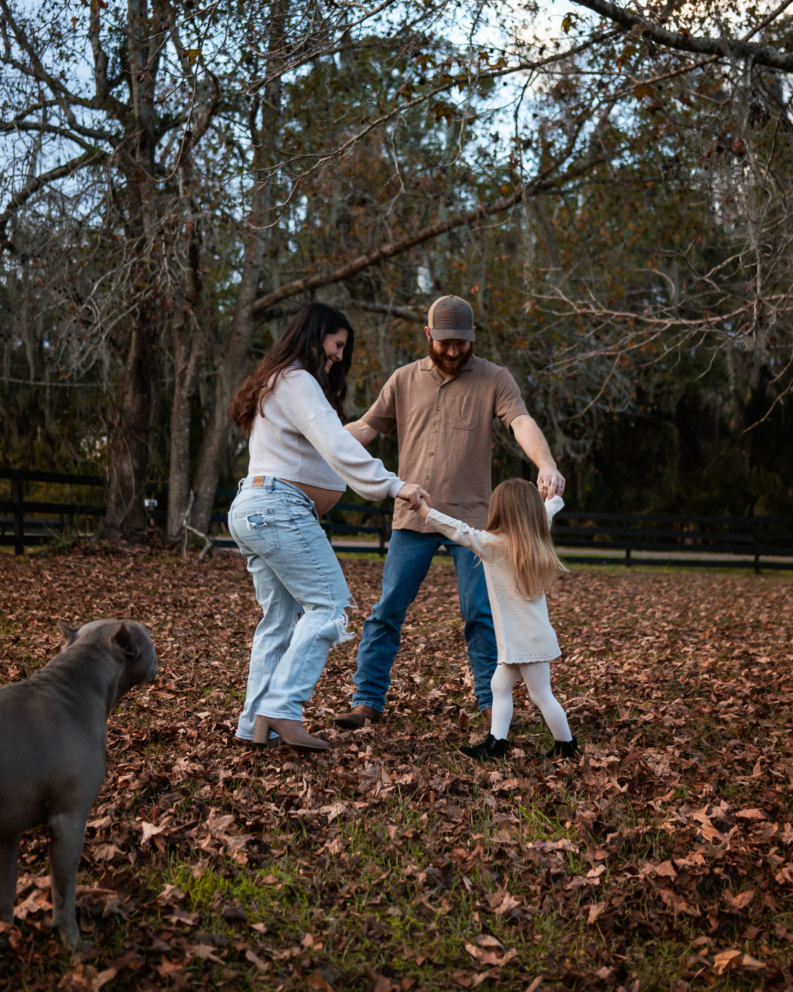 Candid family maternity photo with parents holding hands with child outdoors