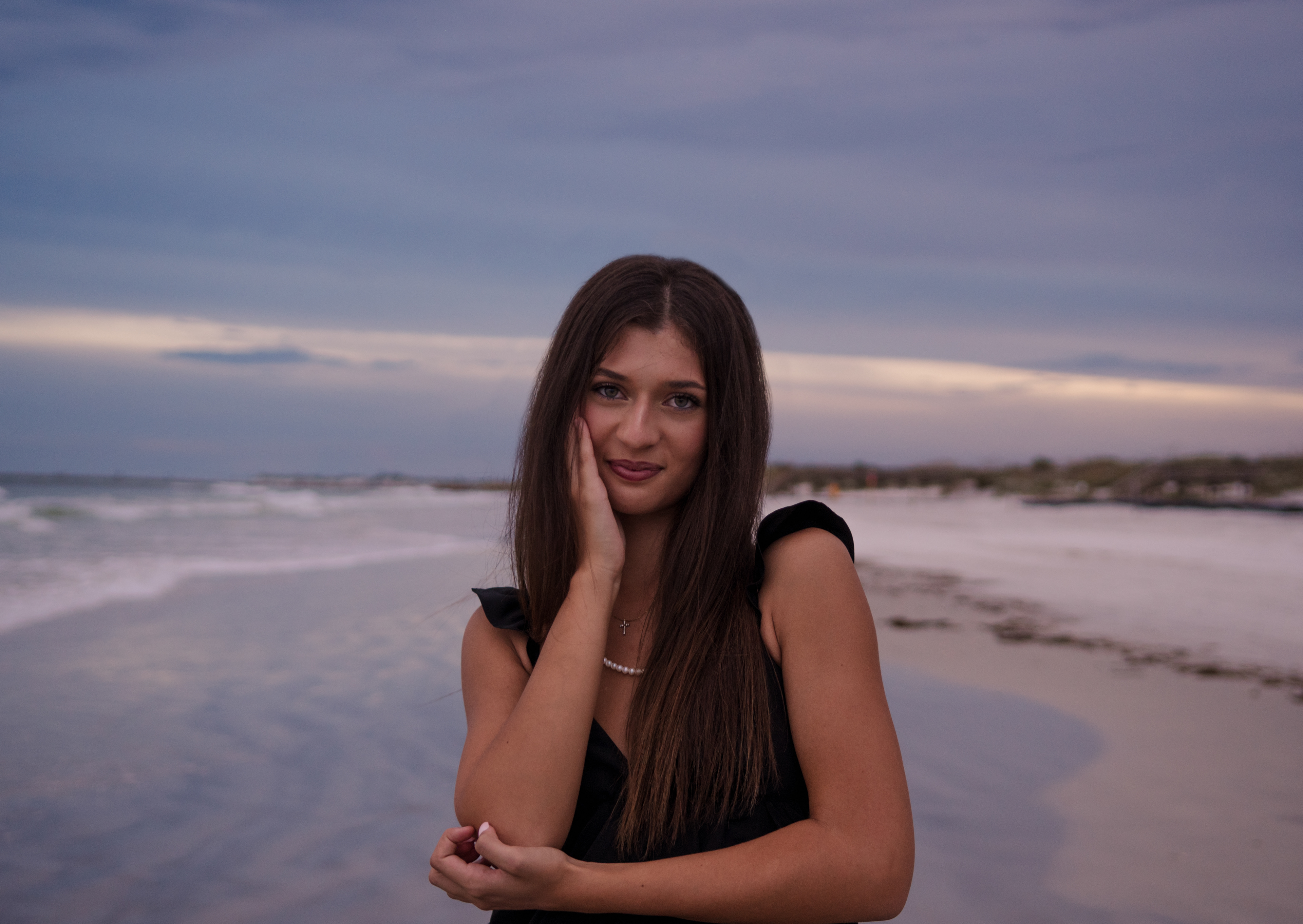 Close-up senior portrait at Ponce Inlet Beach, Mia in a black dress with ocean sunset behind her.