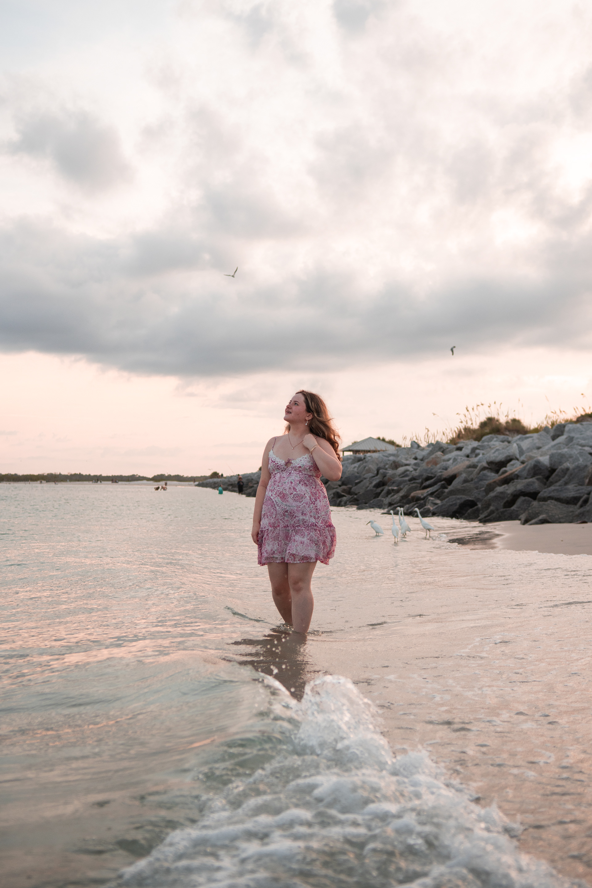 Senior photos at Ponce Inlet Beach, Nelly walking in shallow waves wearing a pink floral dress.