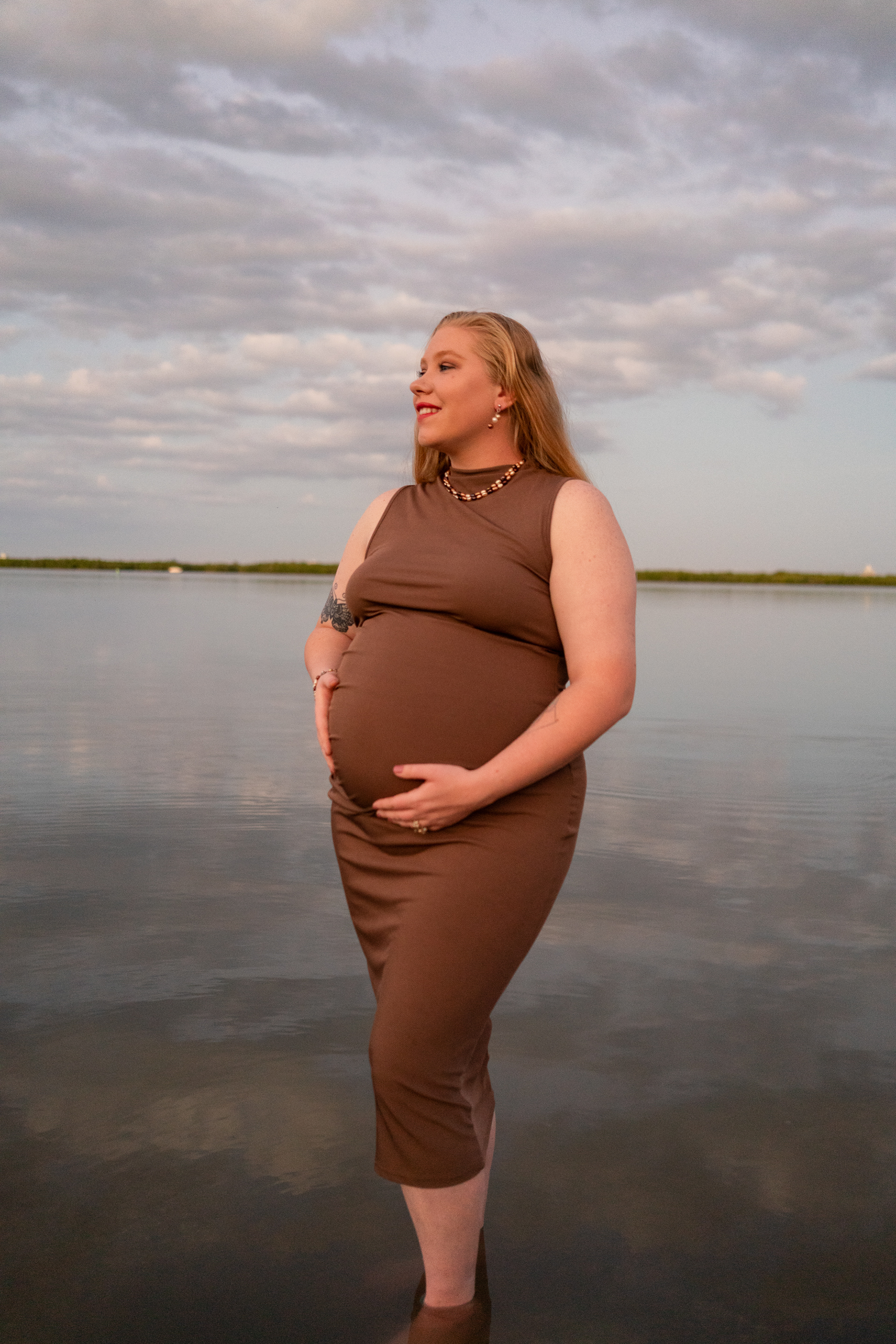 Outdoor maternity photo of pregnant mother standing near the water at dusk