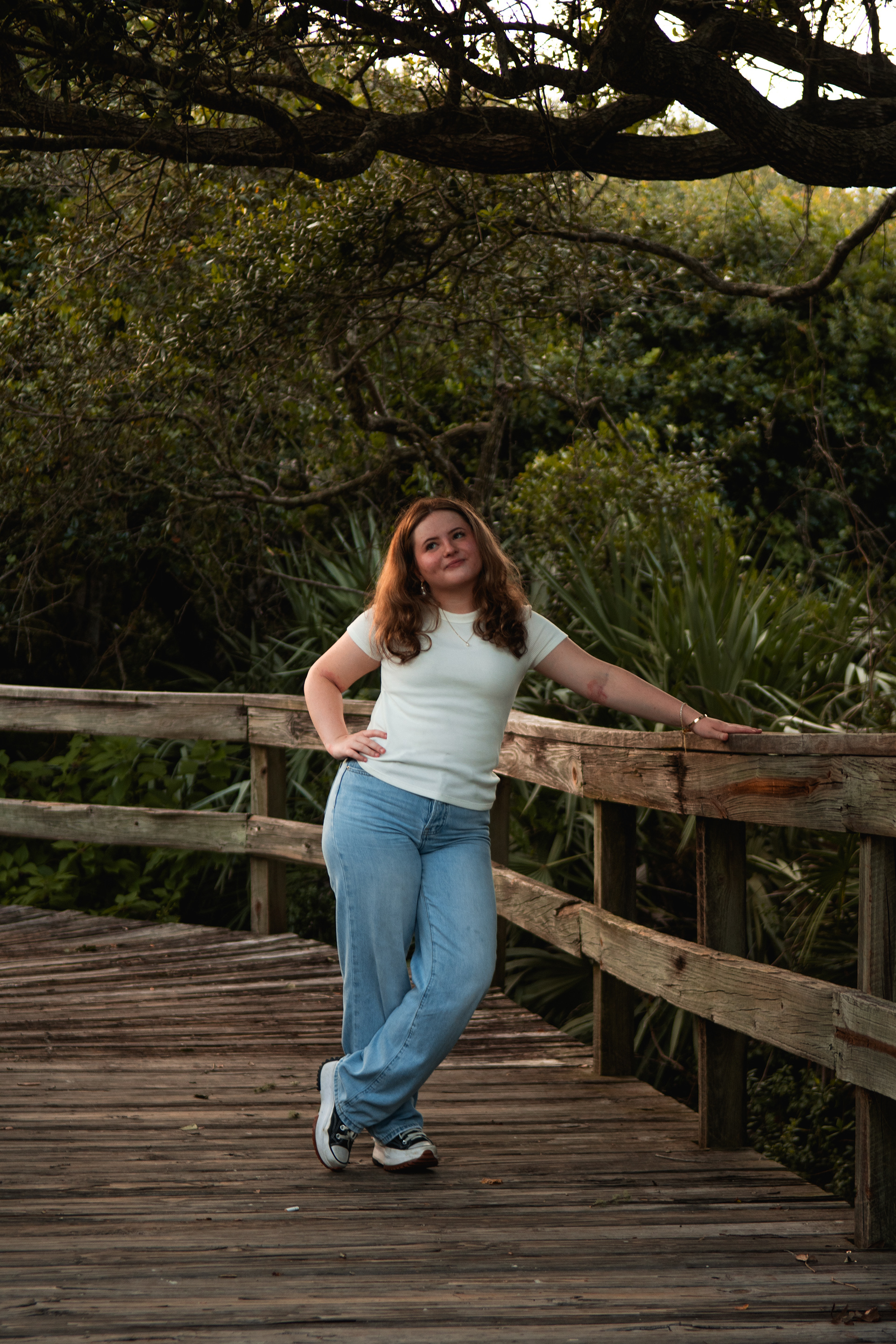 Senior photos in Ponce Inlet, Nelly posing on the boardwalk under shaded oak trees, casual outfit with jeans.