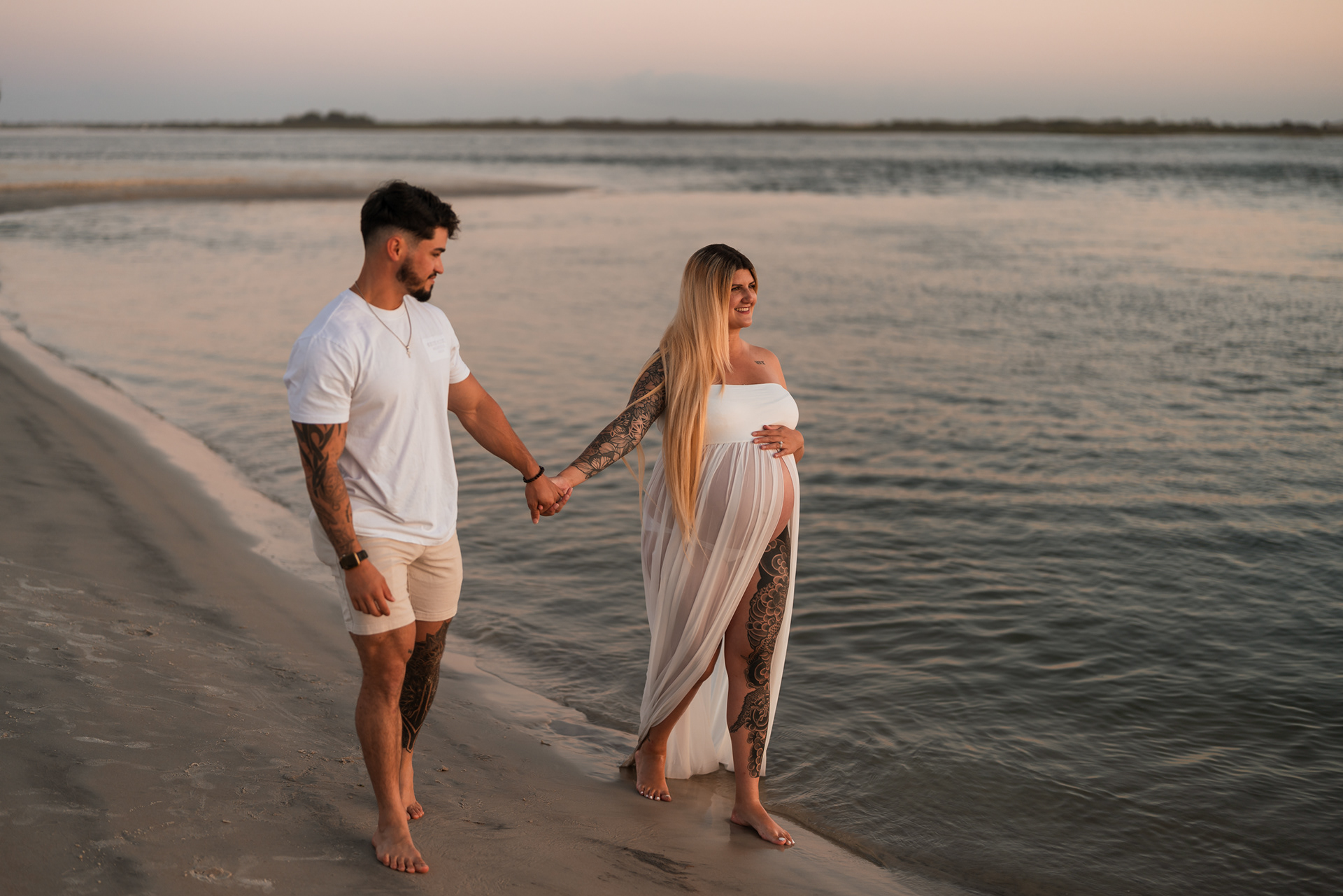 Couple walking along the shoreline during a beach maternity photo session