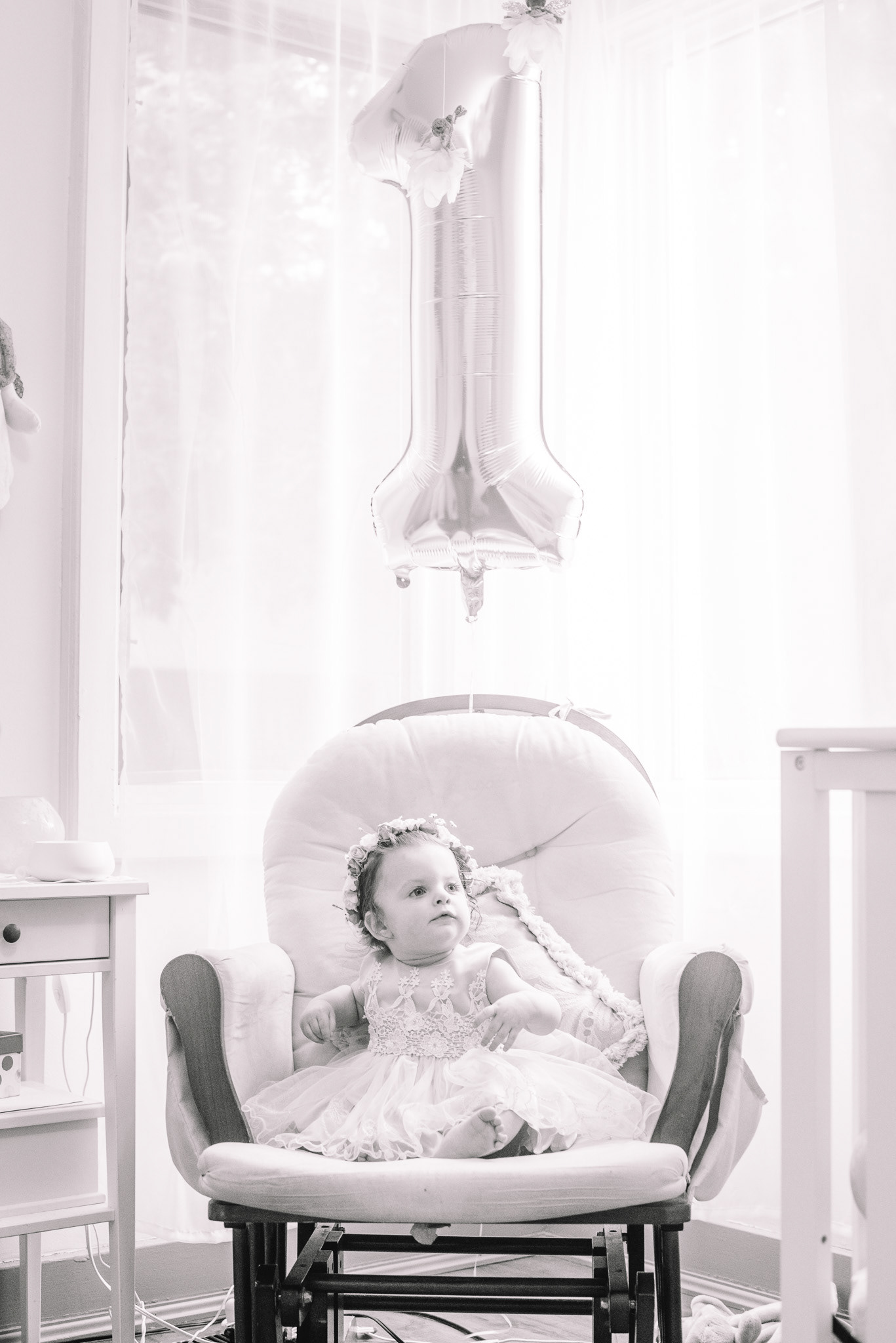 Lilly sitting in a rocking chair with a 'one' balloon.